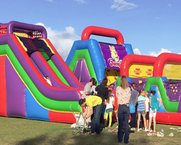Children at colorful inflatable slides with adults watching at a fairground