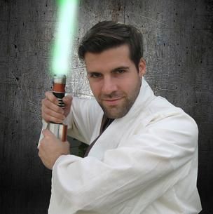 Man in a white robe holding a glowing green lightsaber against a gray background