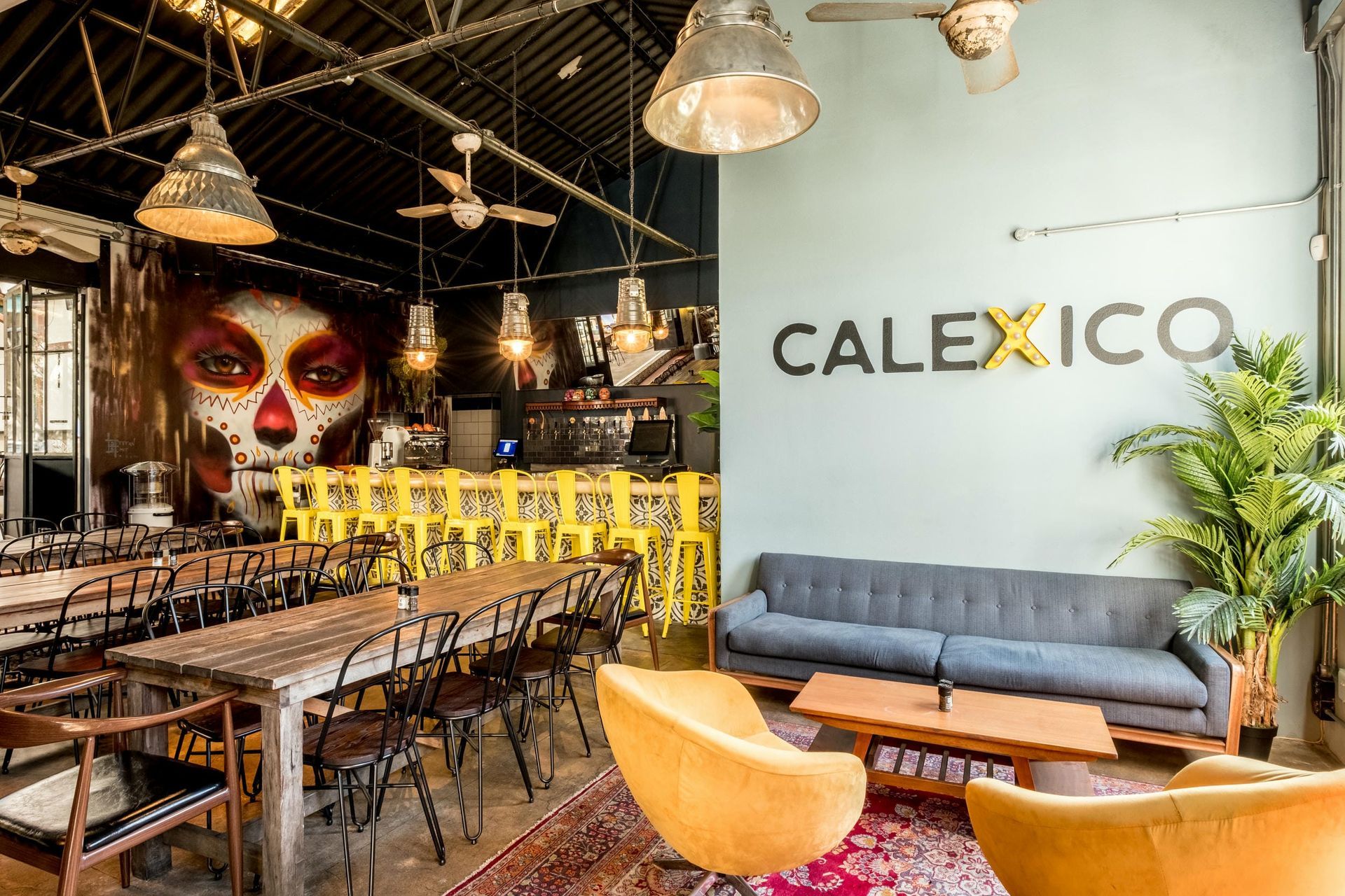 A large room with a couch , chairs , tables and a mural on the wall that says calexico.