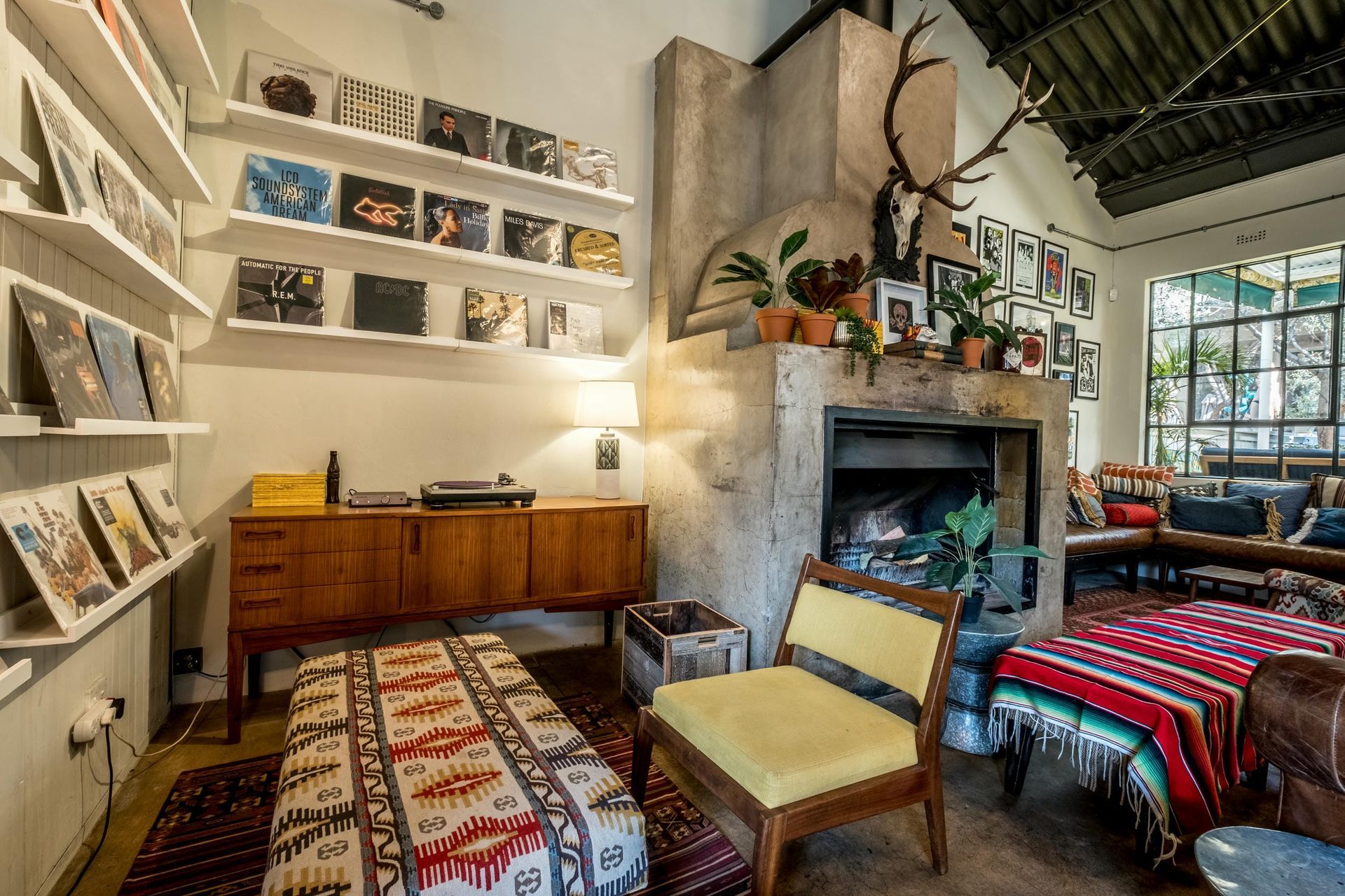 A living room with a fireplace , chairs , ottoman and a record player.