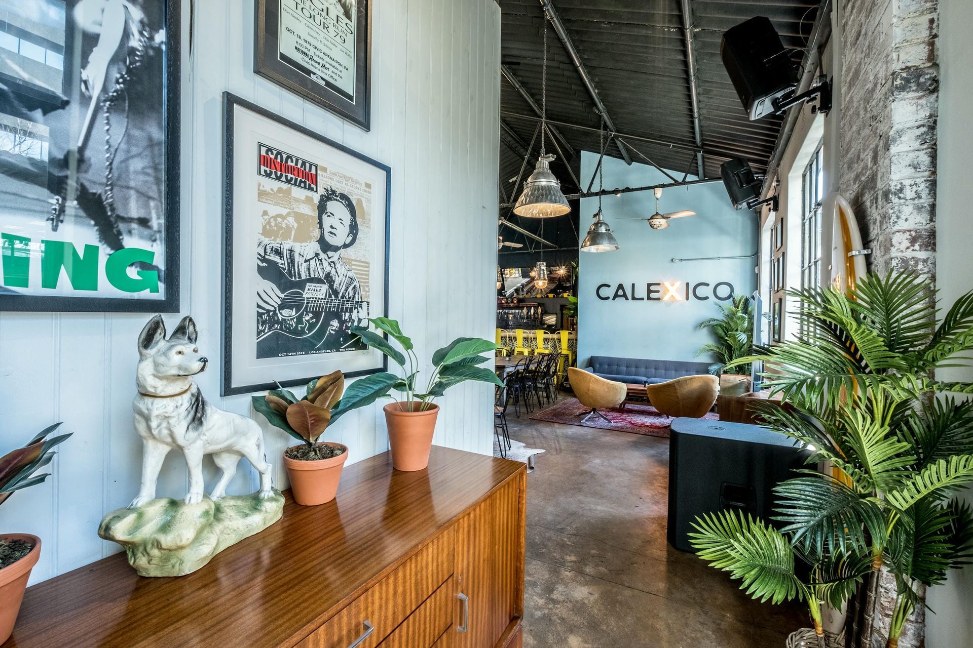 A room with a couch , chairs , potted plants and a statue of a dog on a dresser.