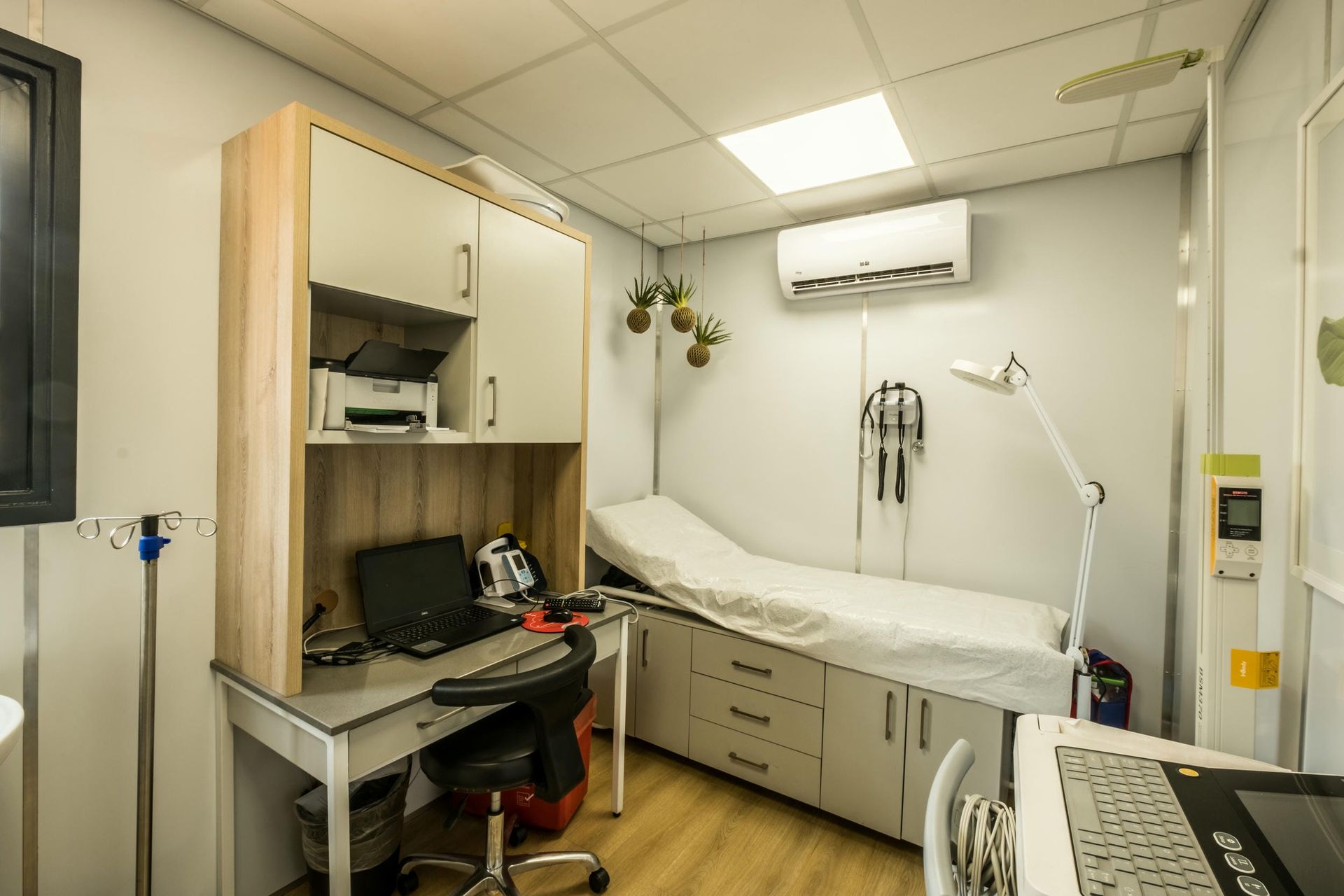 A doctor 's office with a bed , desk , chair and computer.