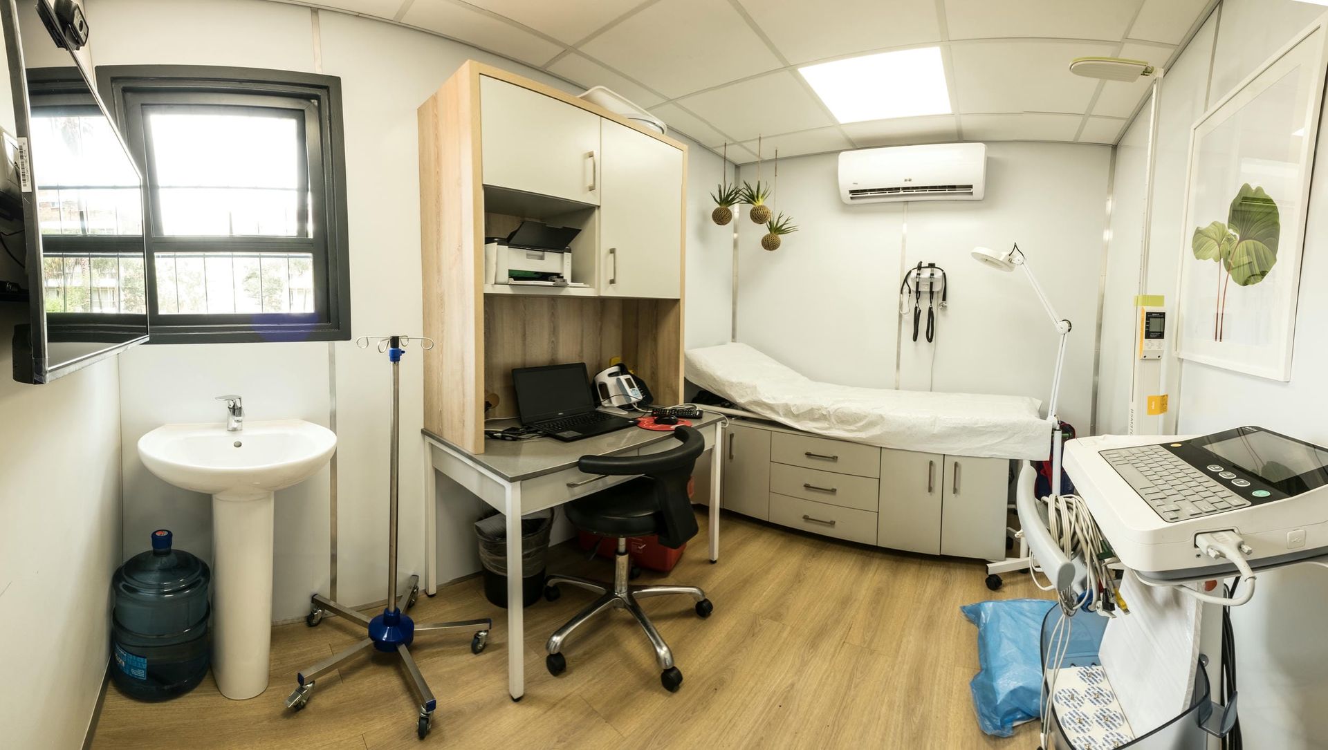 A panoramic view of a doctor 's office with a sink , desk and examination table.