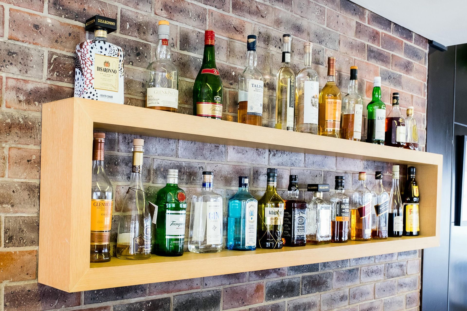 A shelf filled with bottles of liquor against a brick wall.