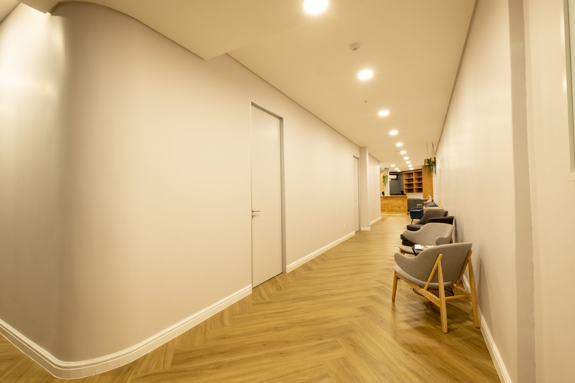 A long hallway with chairs and a door in a building.