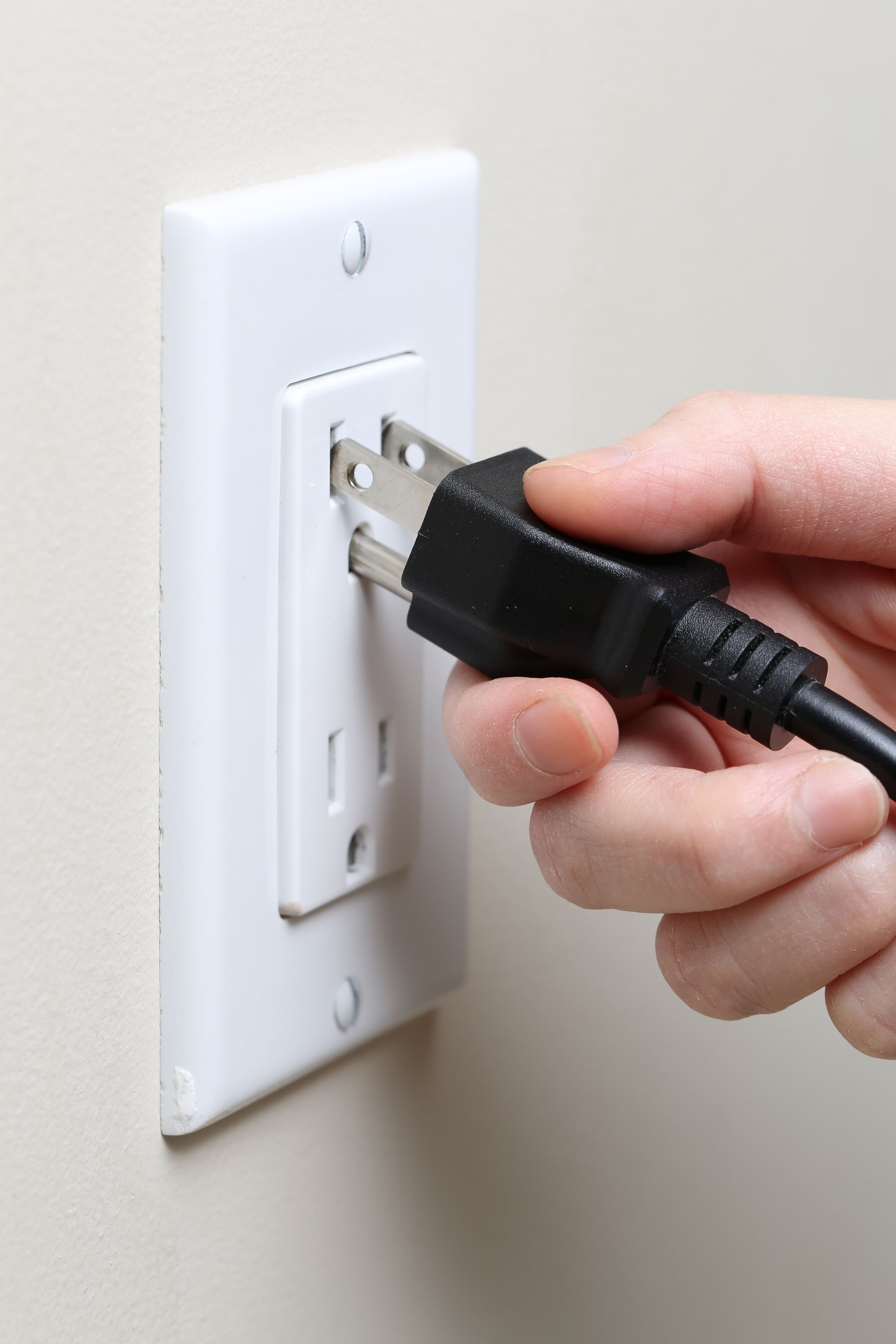 Hand plugging a black power cord into a white wall outlet.