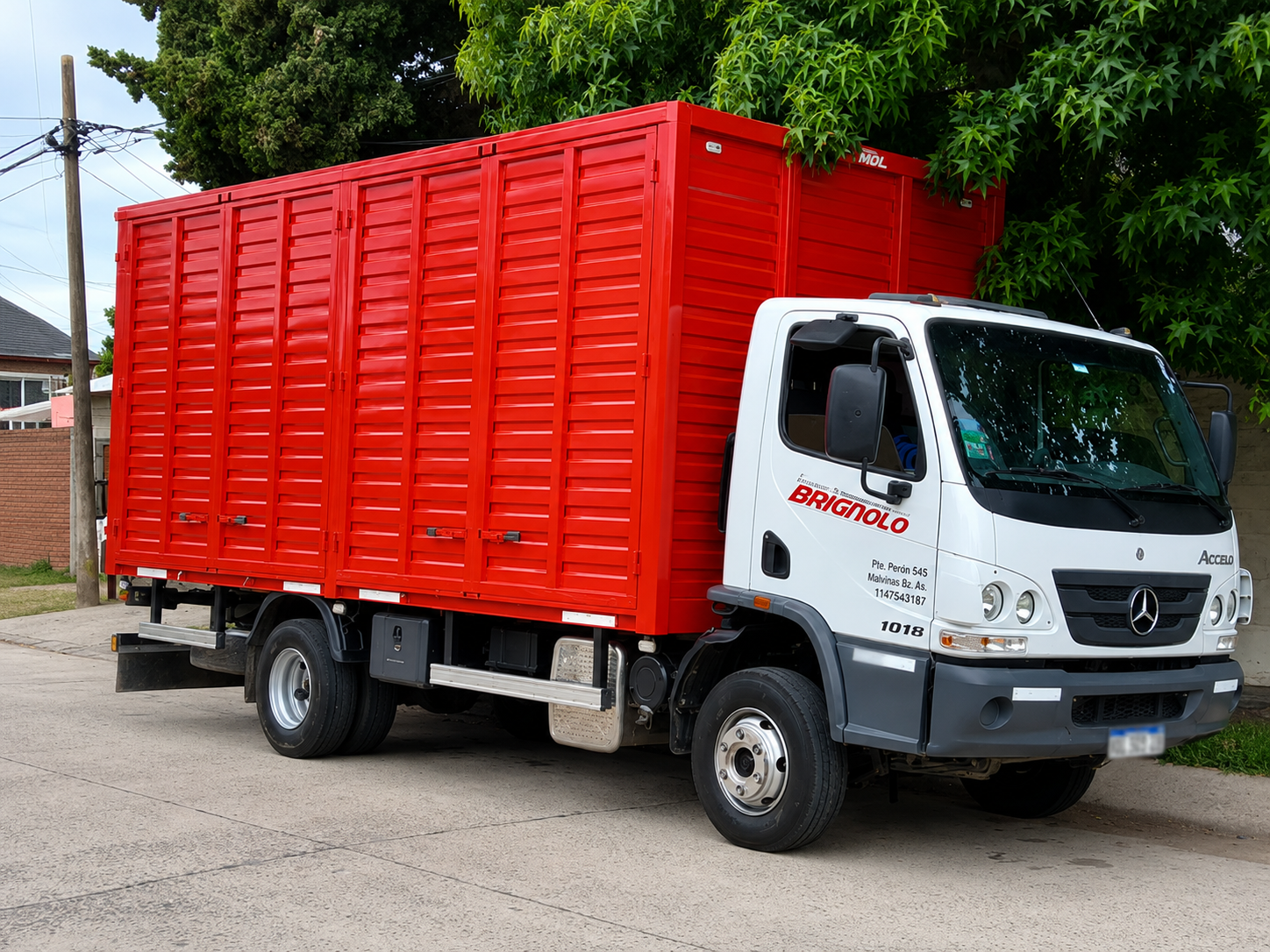 Camión de carga rojo estacionado al aire libre en un terreno de tierra, con cabina blanca y caja de color rojo brillante.