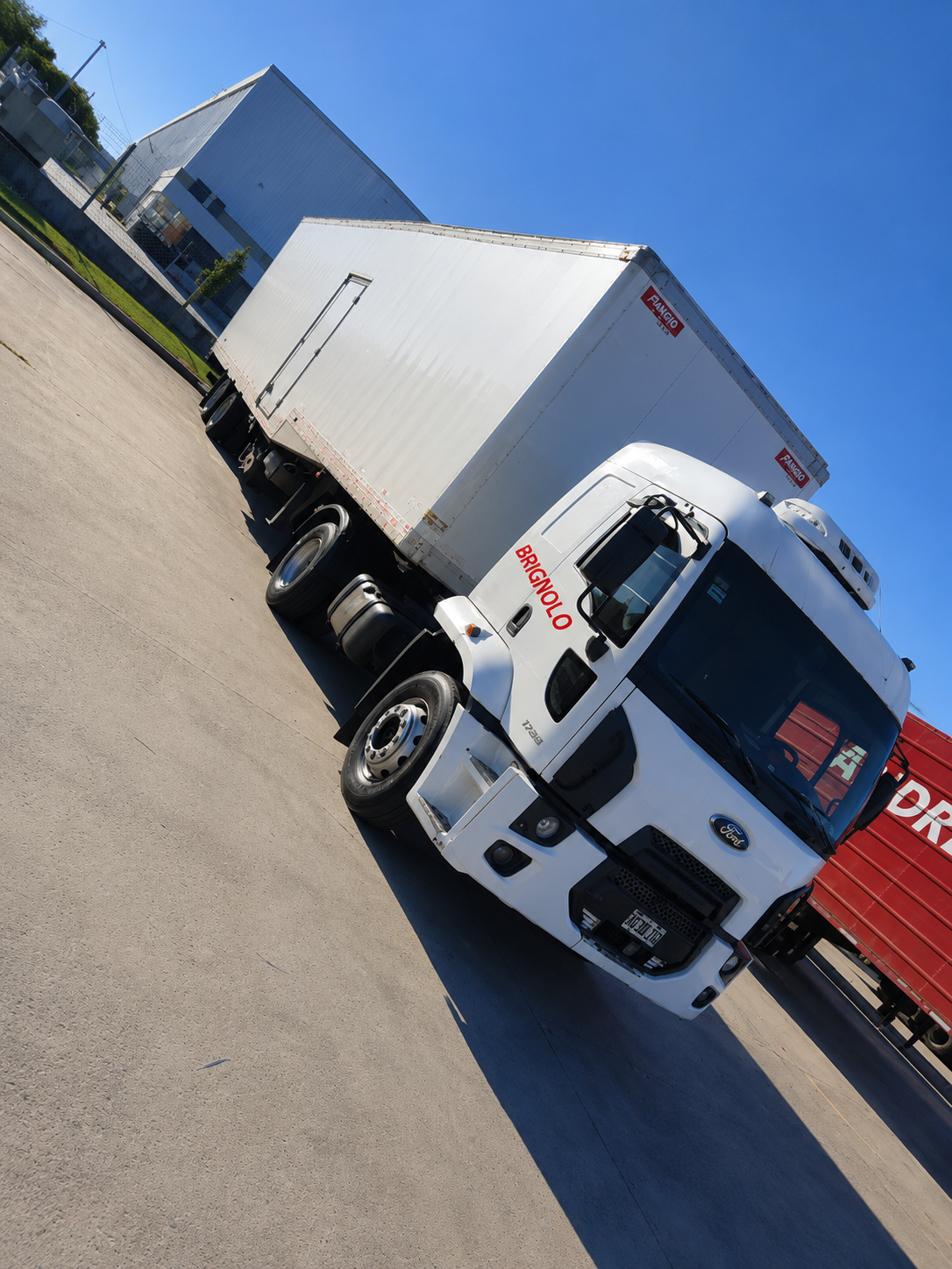 Camión blanco estacionado en ángulo junto a un contenedor de transporte rojo en un lote industrial.
