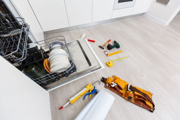 Dishwasher repair with tools scattered on floor.