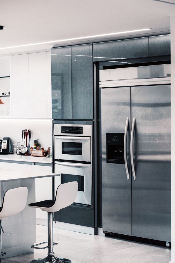 Modern kitchen with stainless steel fridge, built-in ovens, white cabinets, and bar stools.