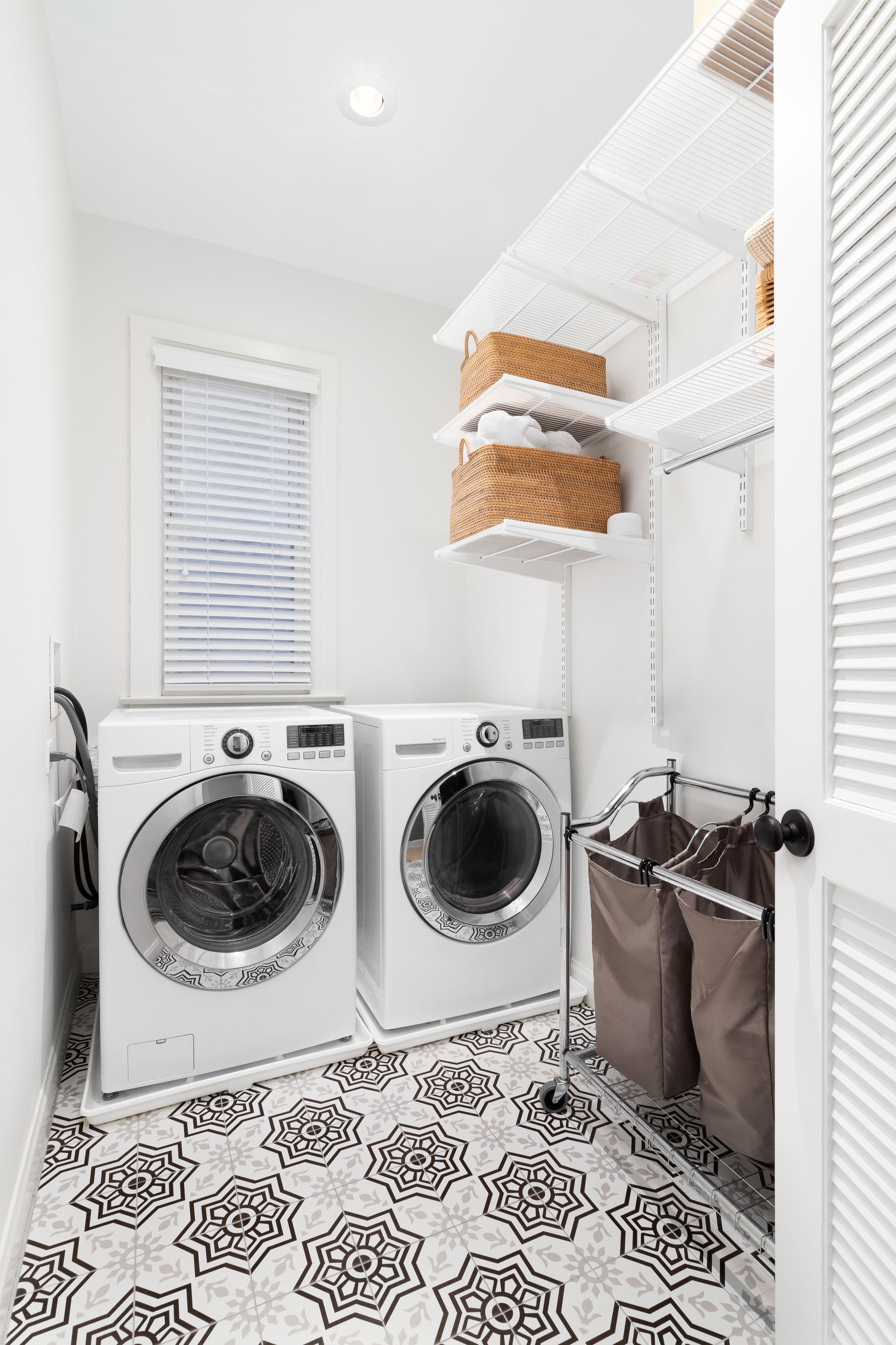 A laundry room with white washer and dryer, a patterned tile floor, and organized shelving on the wall. A laundry room with white washer and dryer, a patterned tile floor, and organized shelving on the wall.