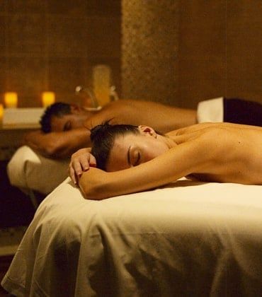 Two people receiving massages on treatment tables in a dimly lit spa room