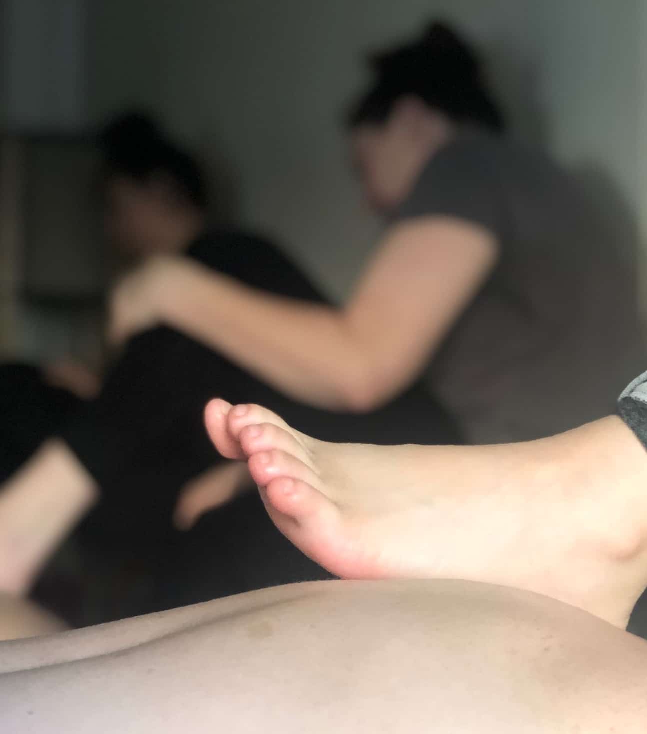 Close-up of a foot in the foreground with two blurred people seated in the background on a soft surface