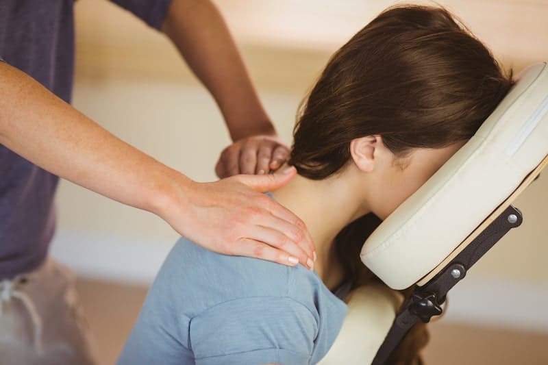 Massage therapist working on a seated person’s neck and shoulders in a clinic room