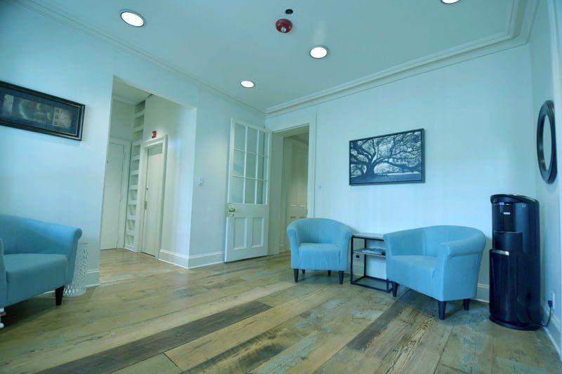 Bright waiting room with blue chairs, wood floors, recessed lights, and a hallway entrance