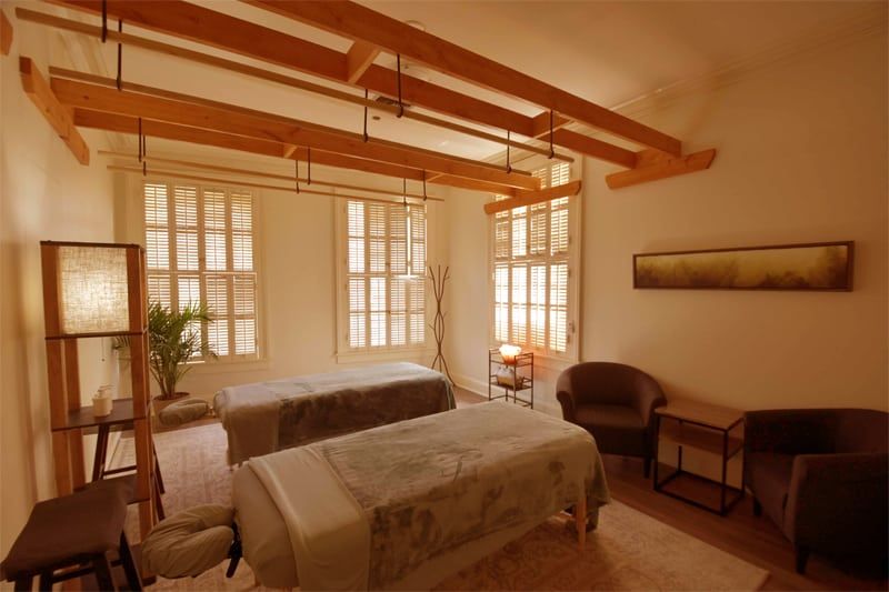 Cozy bedroom with a bed, warm wood beams, shutters, and two chairs by a small table