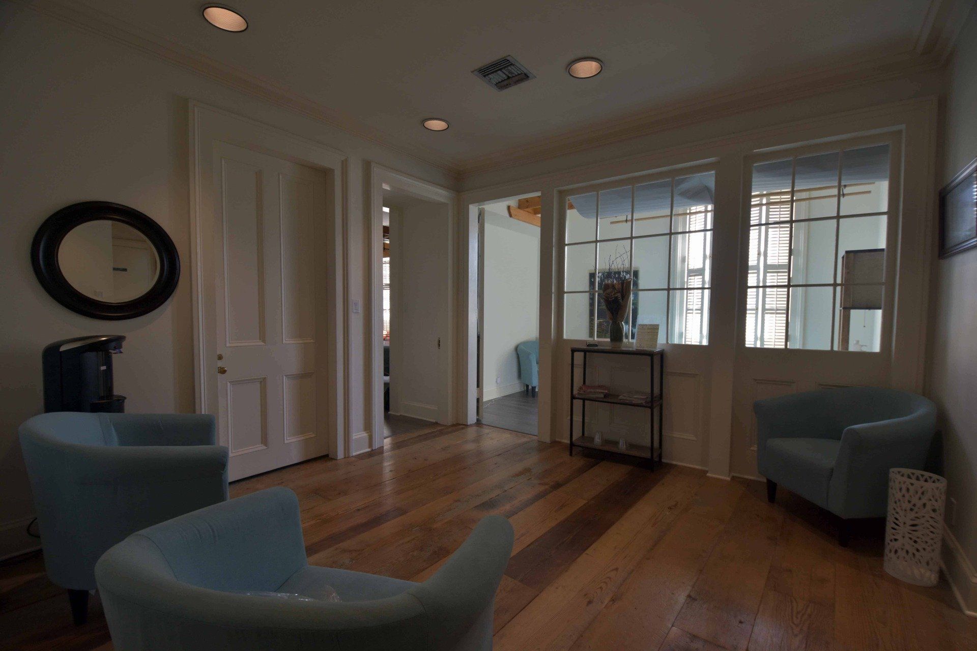 Bright sunroom with wood floors, blue chairs, and large windows facing a neighboring house
