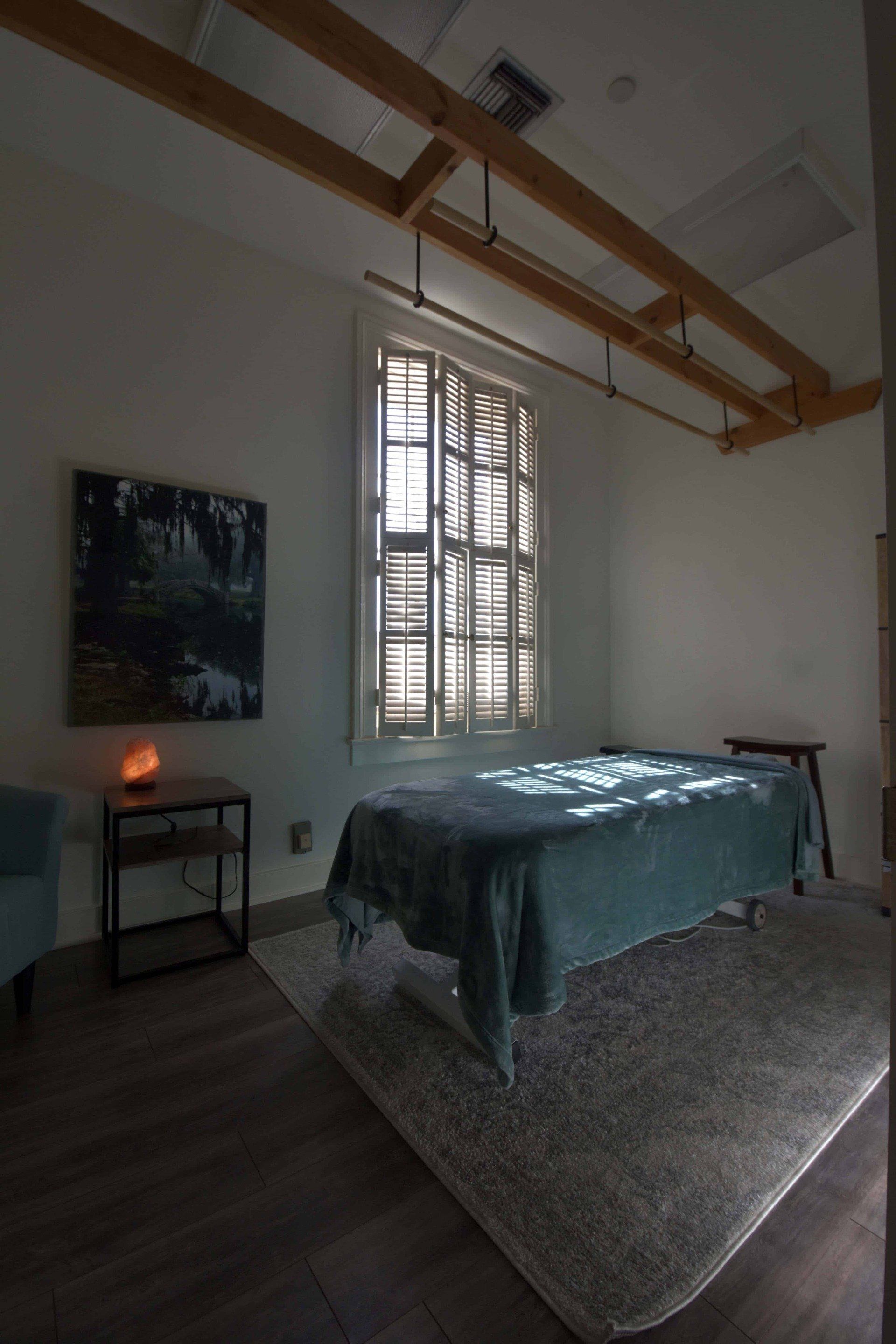 Minimal bedroom with a made bed, window shutters, rug, wall art, and exposed ceiling beams.