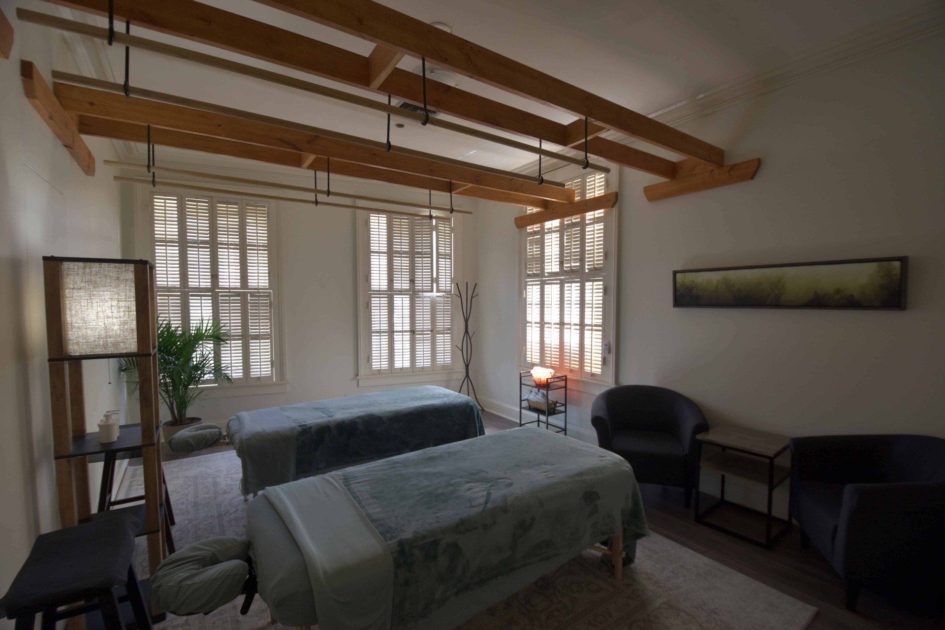Bright bedroom with a bed, wood ceiling beams, large windows, and dark chairs