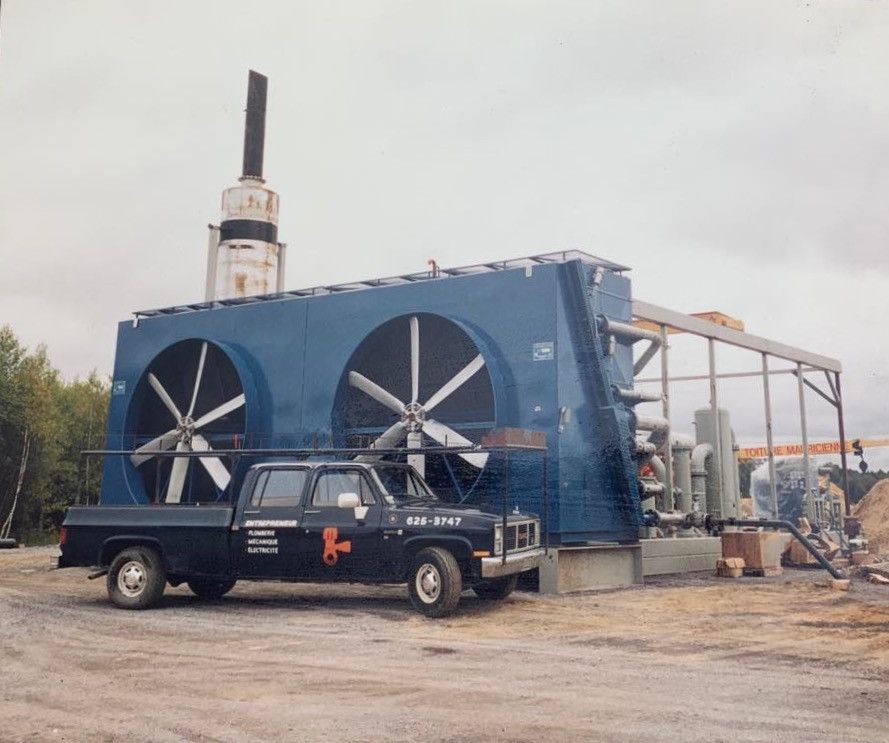 Grande unité de refroidissement industrielle bleue avec deux ventilateurs, camionnette noire garée devant.