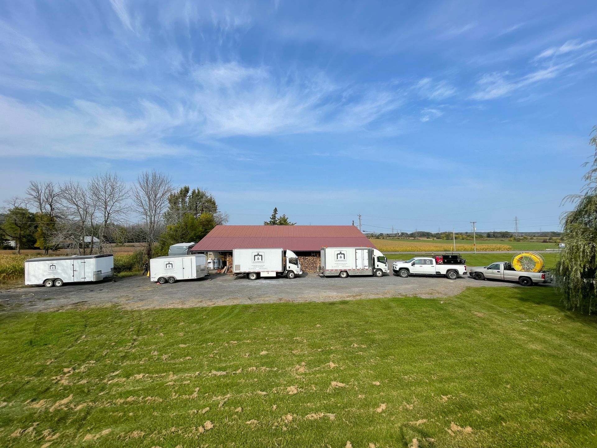 Vehicles parked in front of a red-roofed building on a green grassy field under a blue sky.