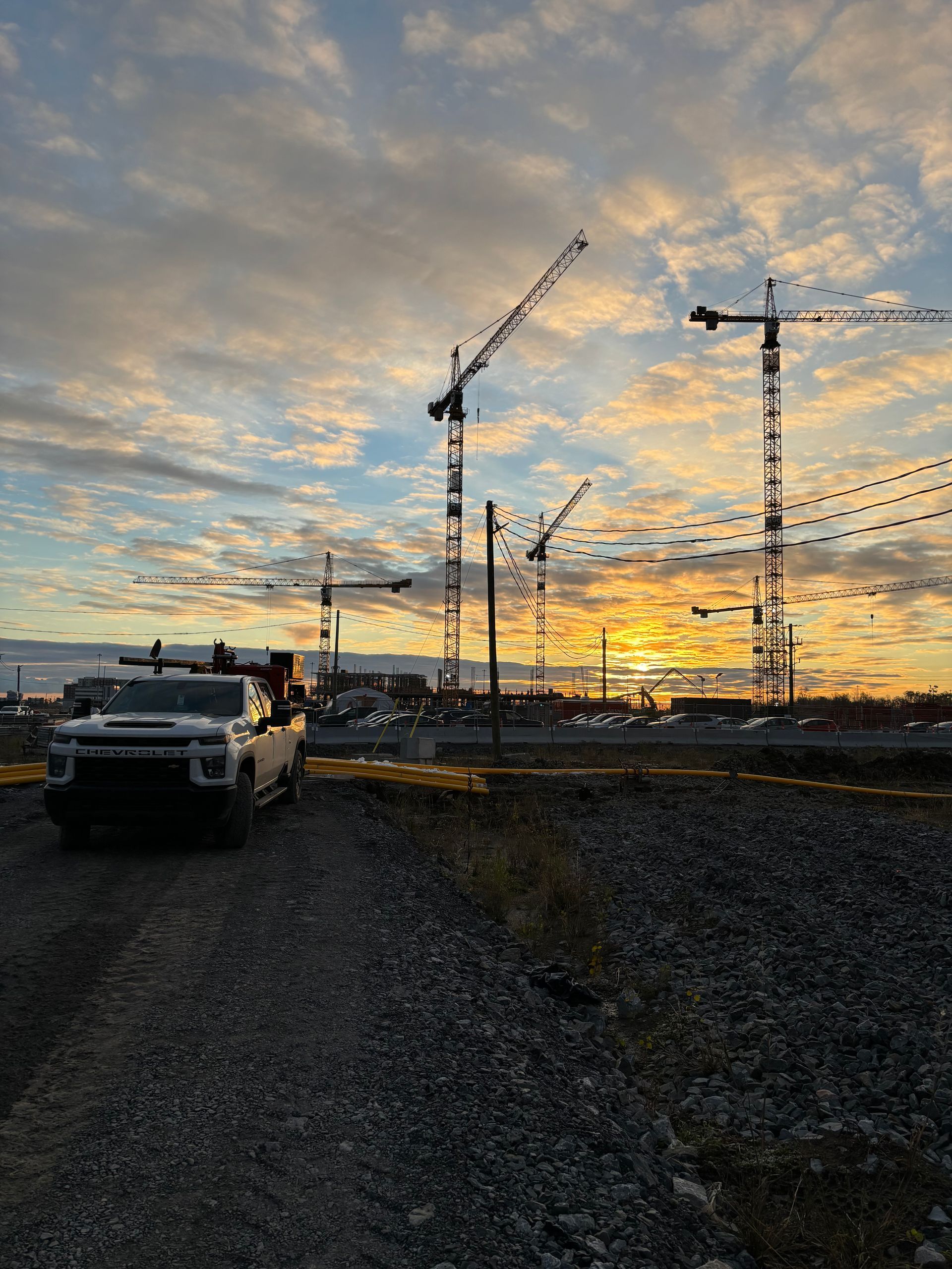 Sunset over construction site with cranes and a truck.