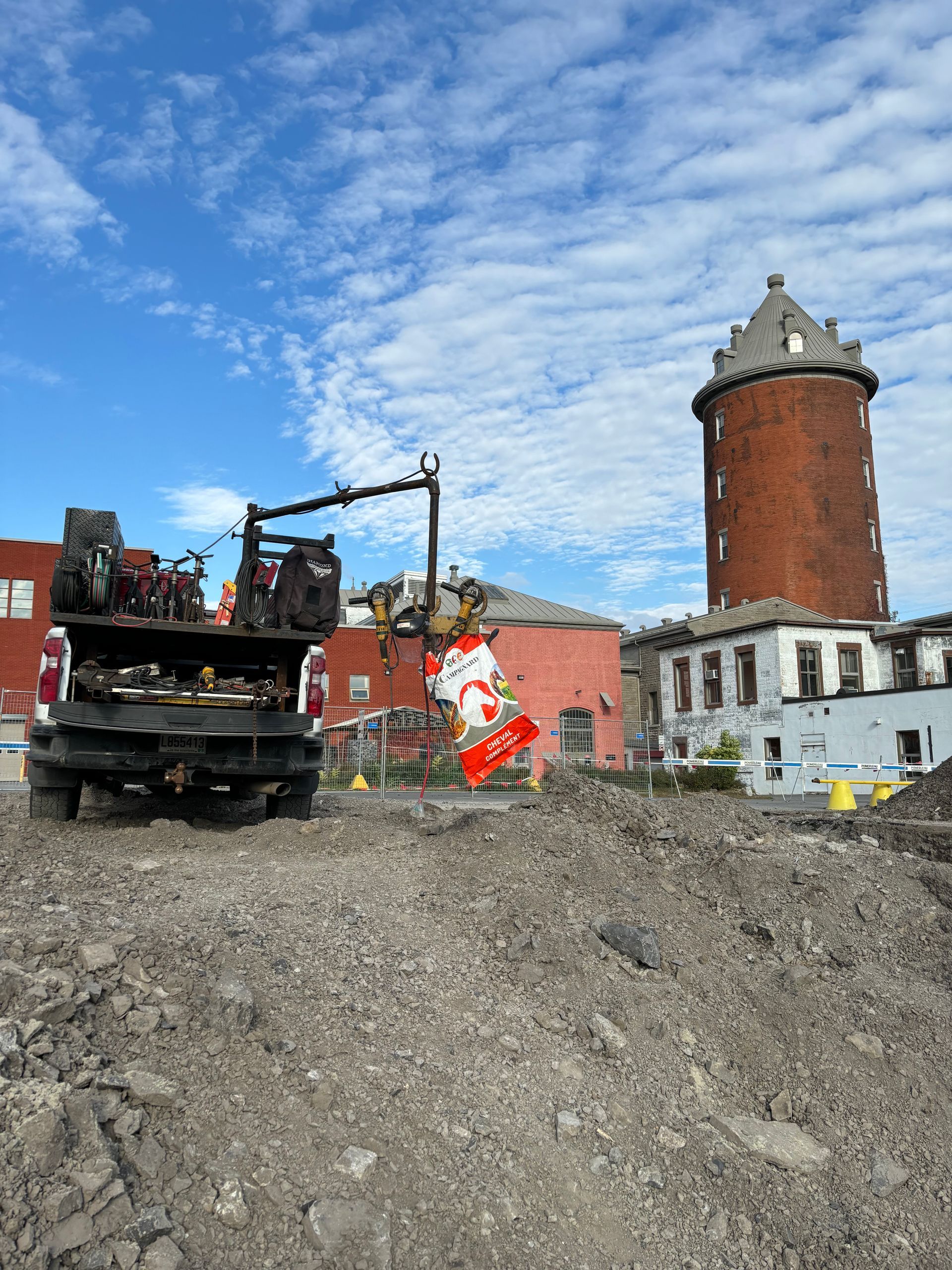 A truck with a crane in front of a brick water tower. A demolition site with blue sky.