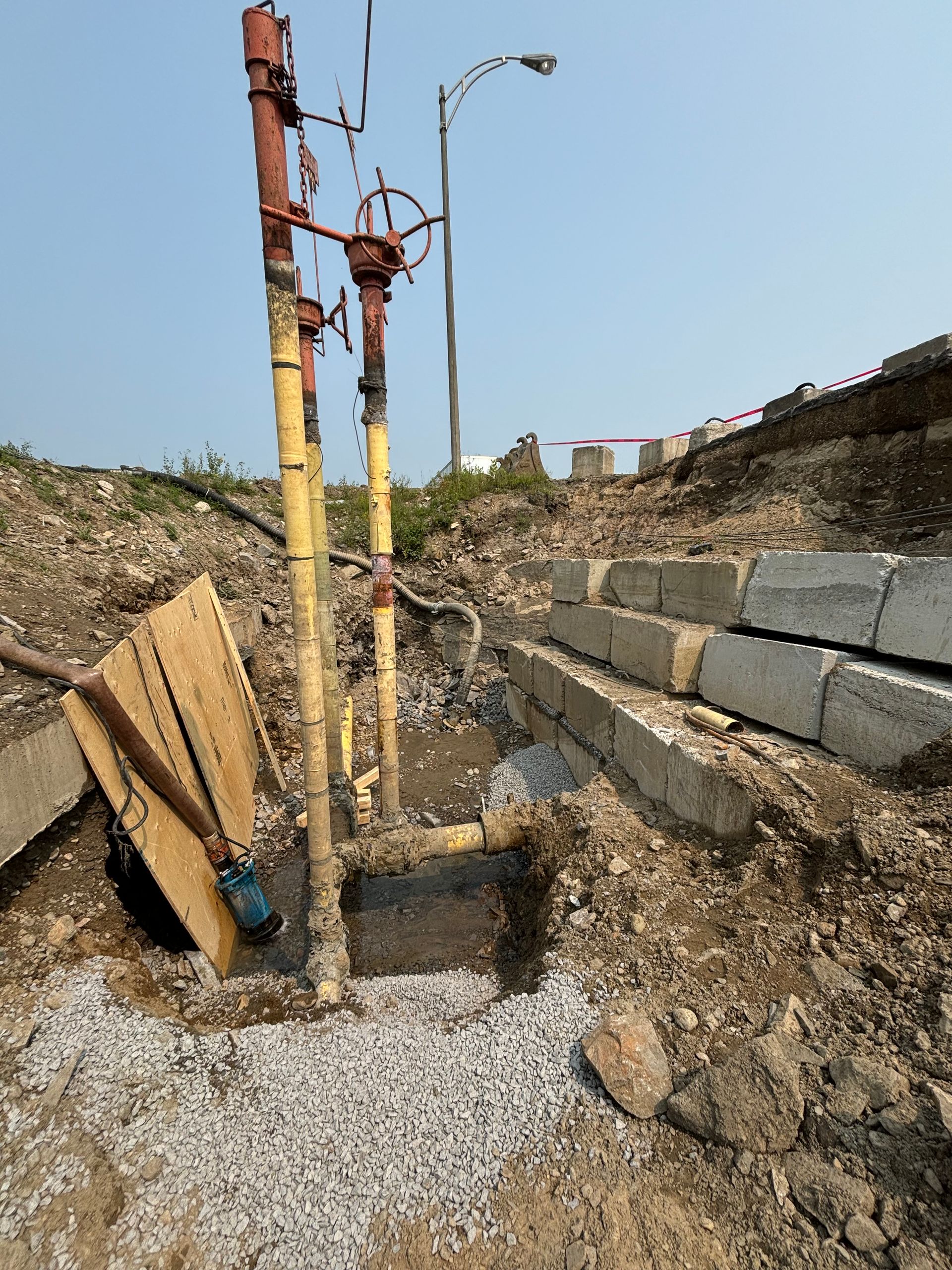 Excavated utilities with yellow pipes, red valves, gravel, and concrete blocks outdoors.