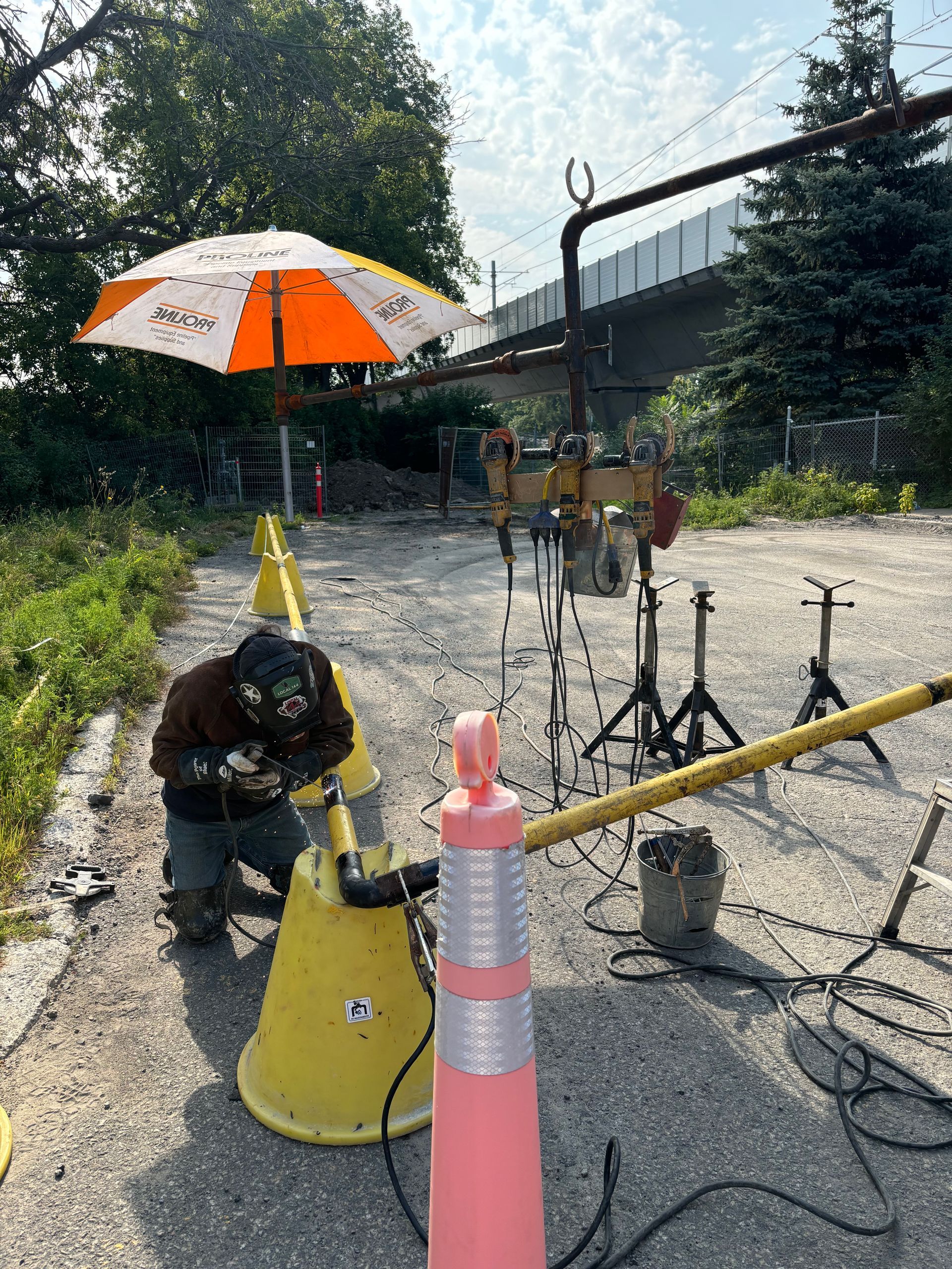 Welder working outside near construction barriers and an umbrella.