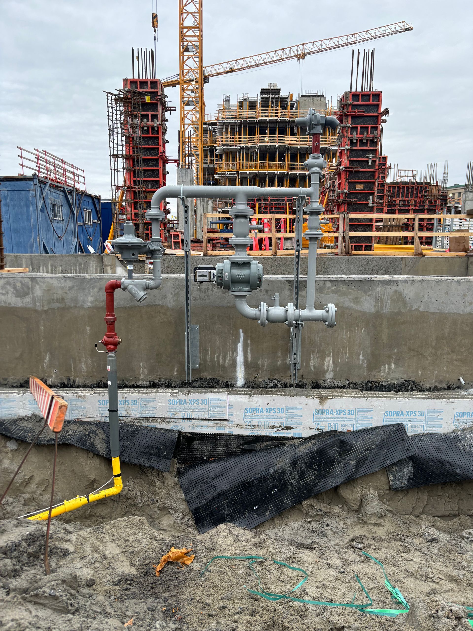 Gas pipes and valves installed at a construction site with building frames and a crane in the background.