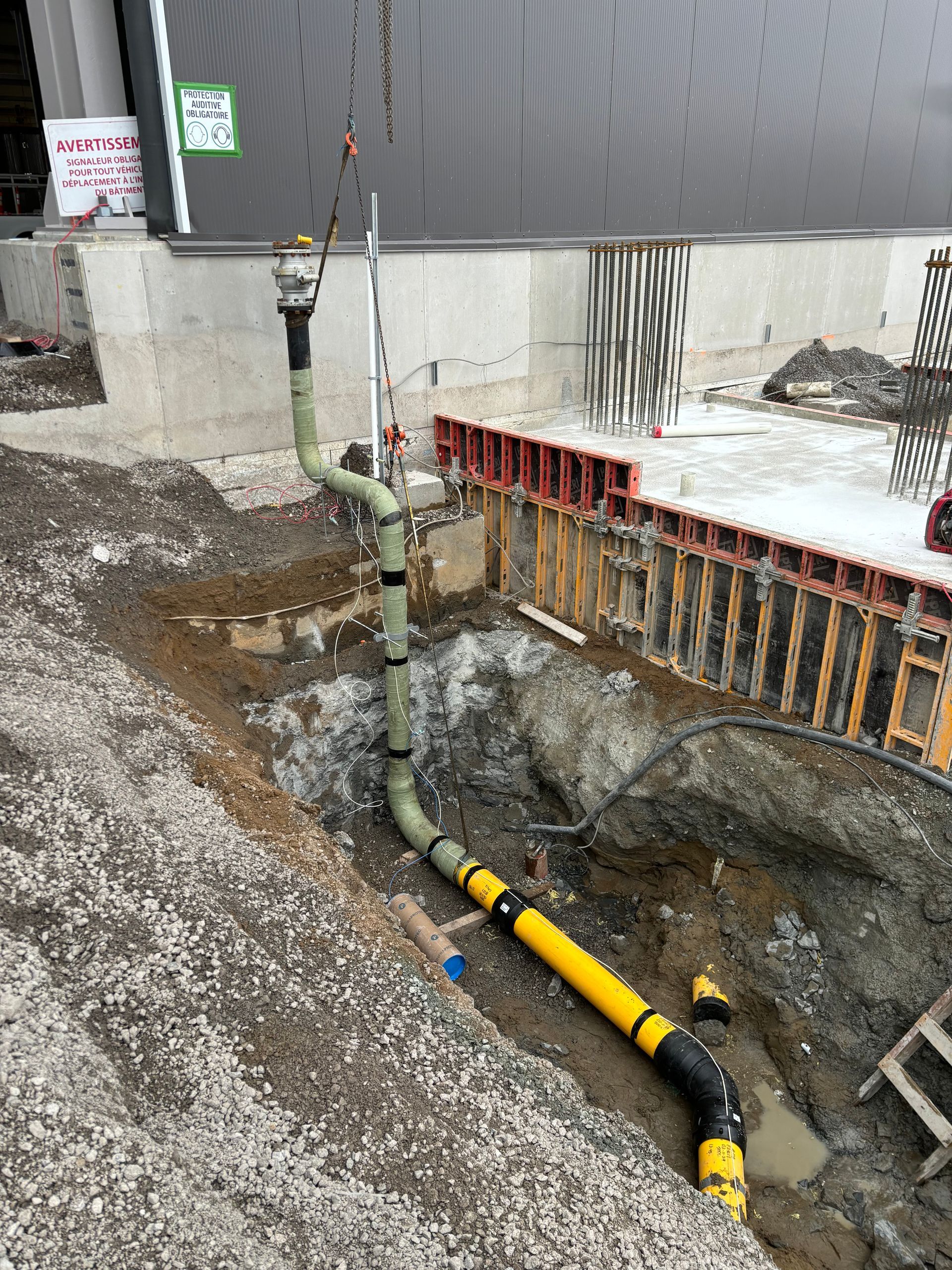 Construction site. A long, yellow and black pipe is lifted from a trench by a crane.