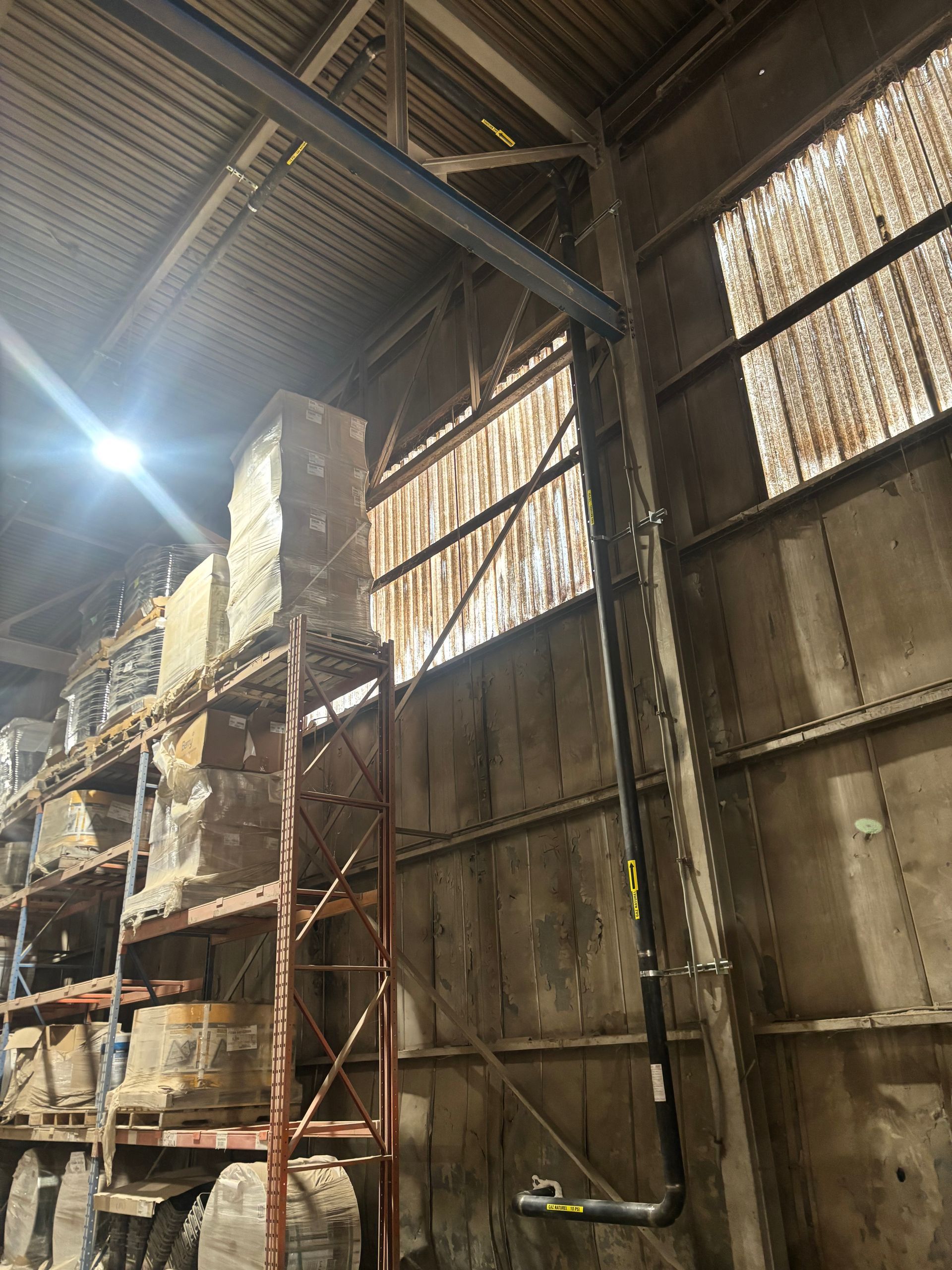 Interior of a warehouse with tall shelves holding stone slabs, sunlight streams through side windows.