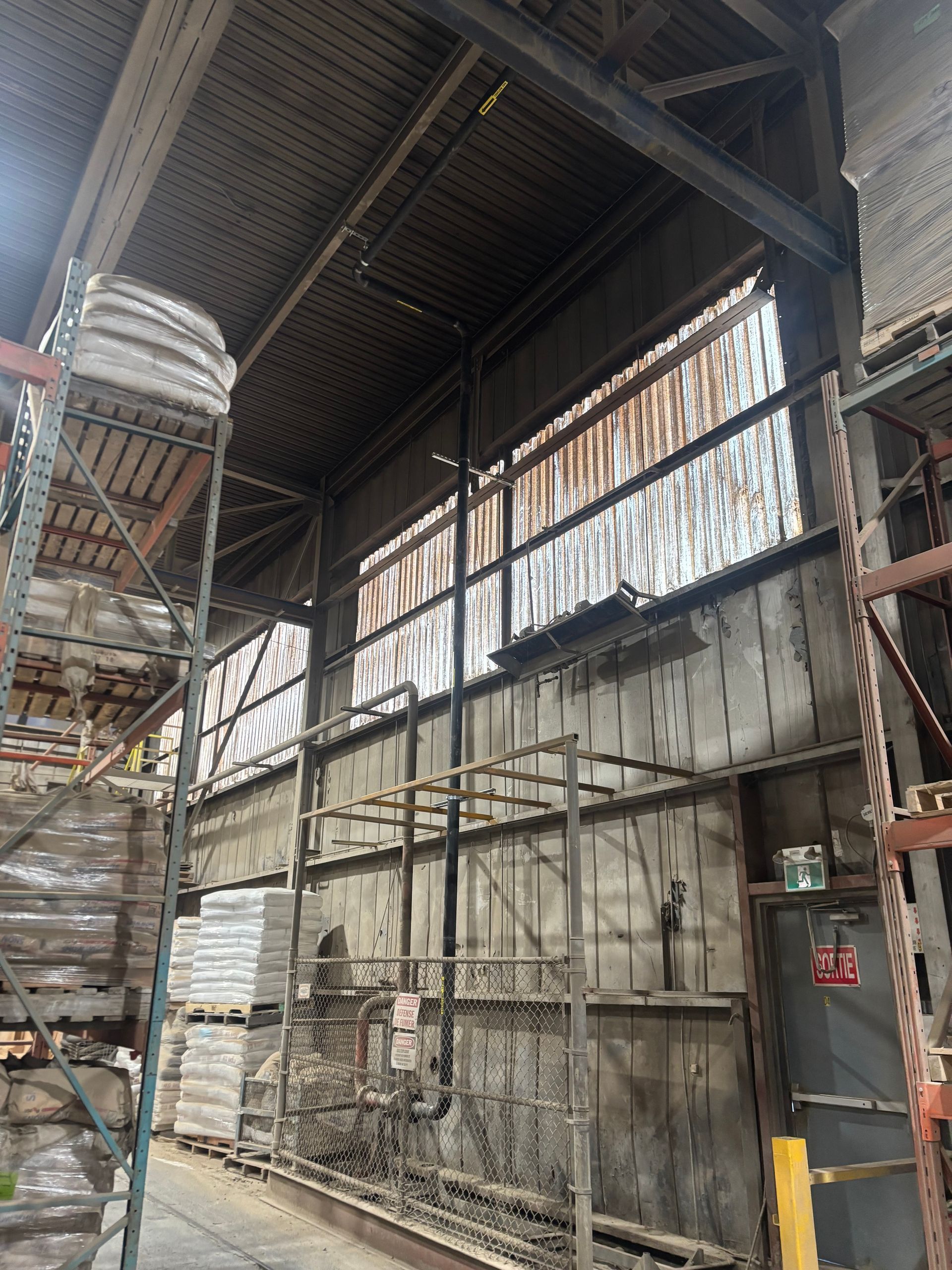 Warehouse interior with high ceilings, steel beams, and stacked materials on shelves.
