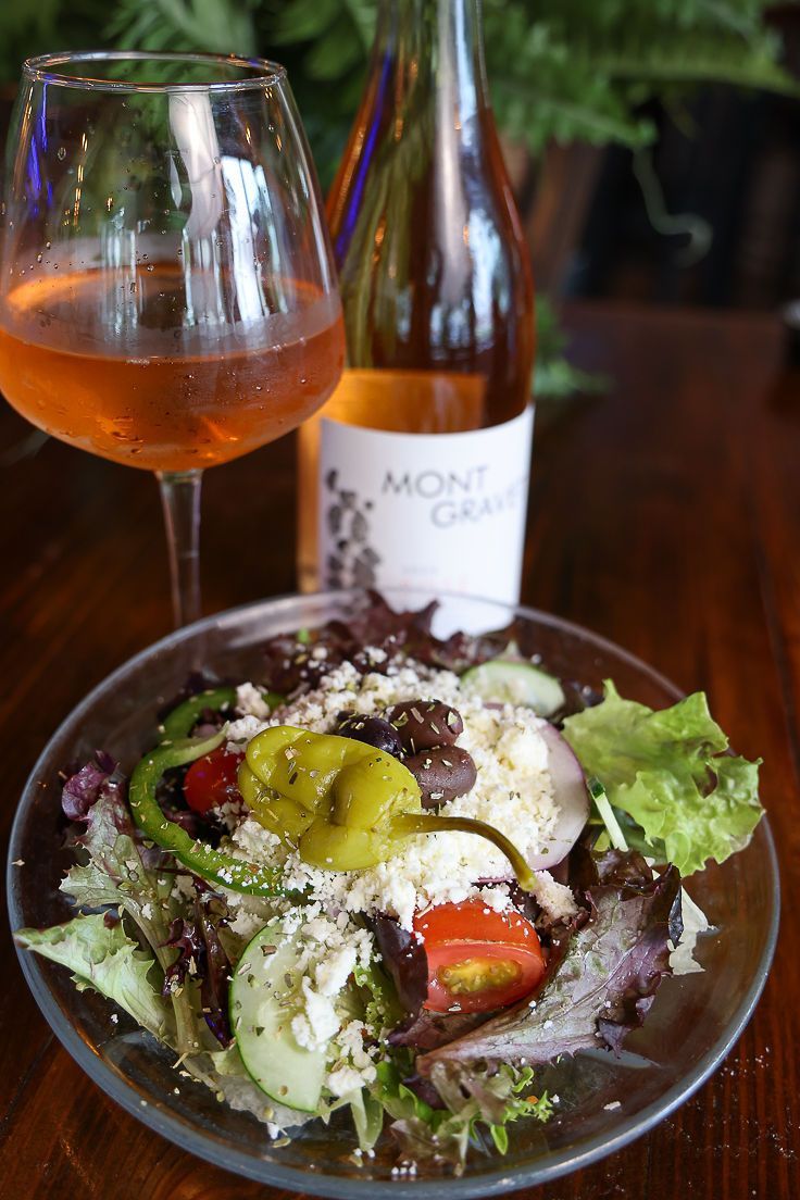 A salad on a plate next to a glass of wine and a bottle of wine.