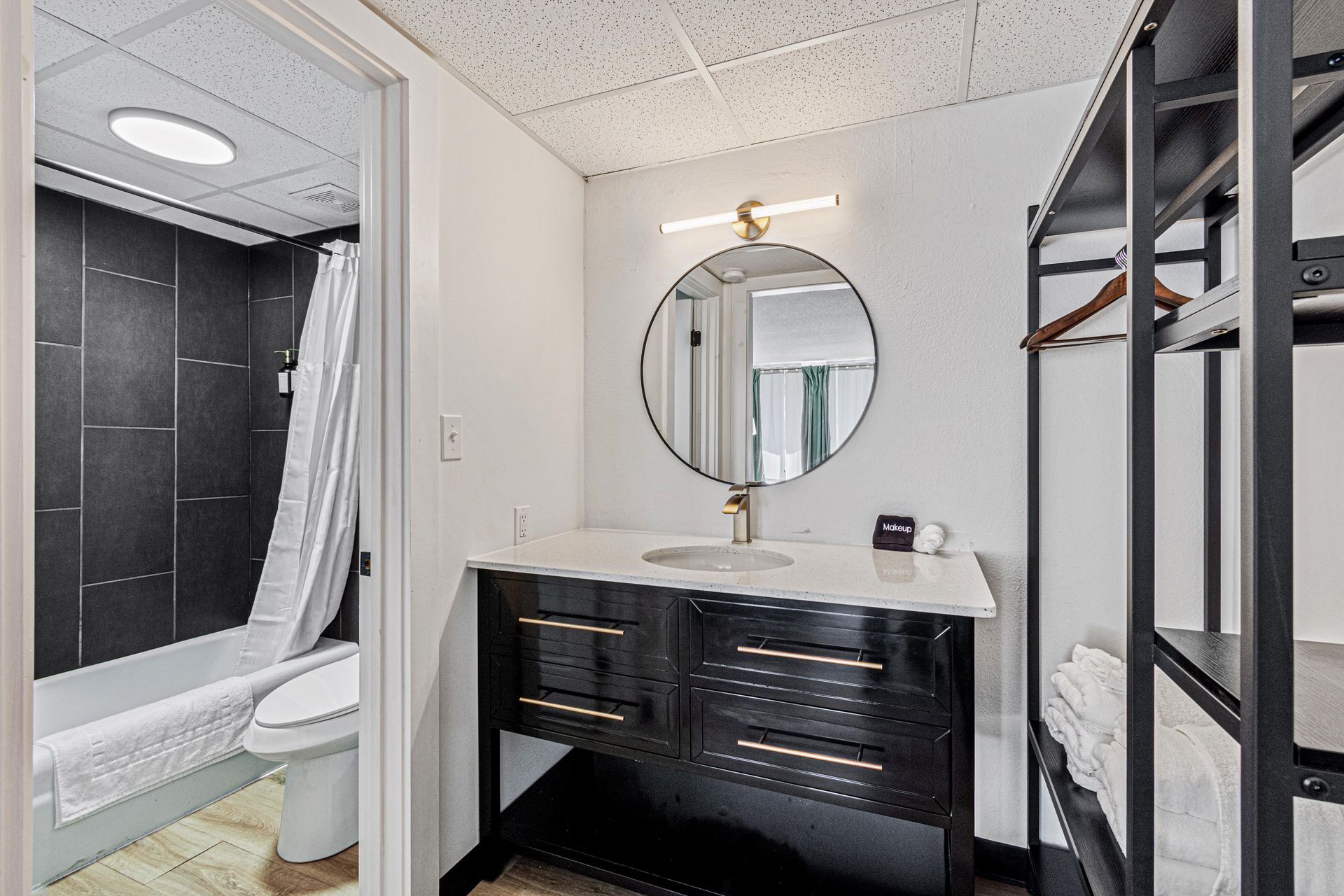 Bathroom with black vanity, round mirror, white countertop, and shower.