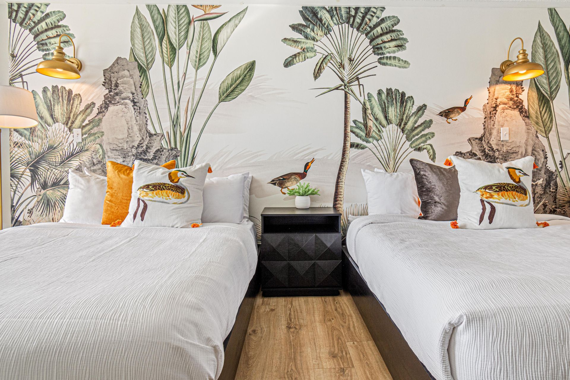 Twin beds with decorative pillows against a botanical mural wall.