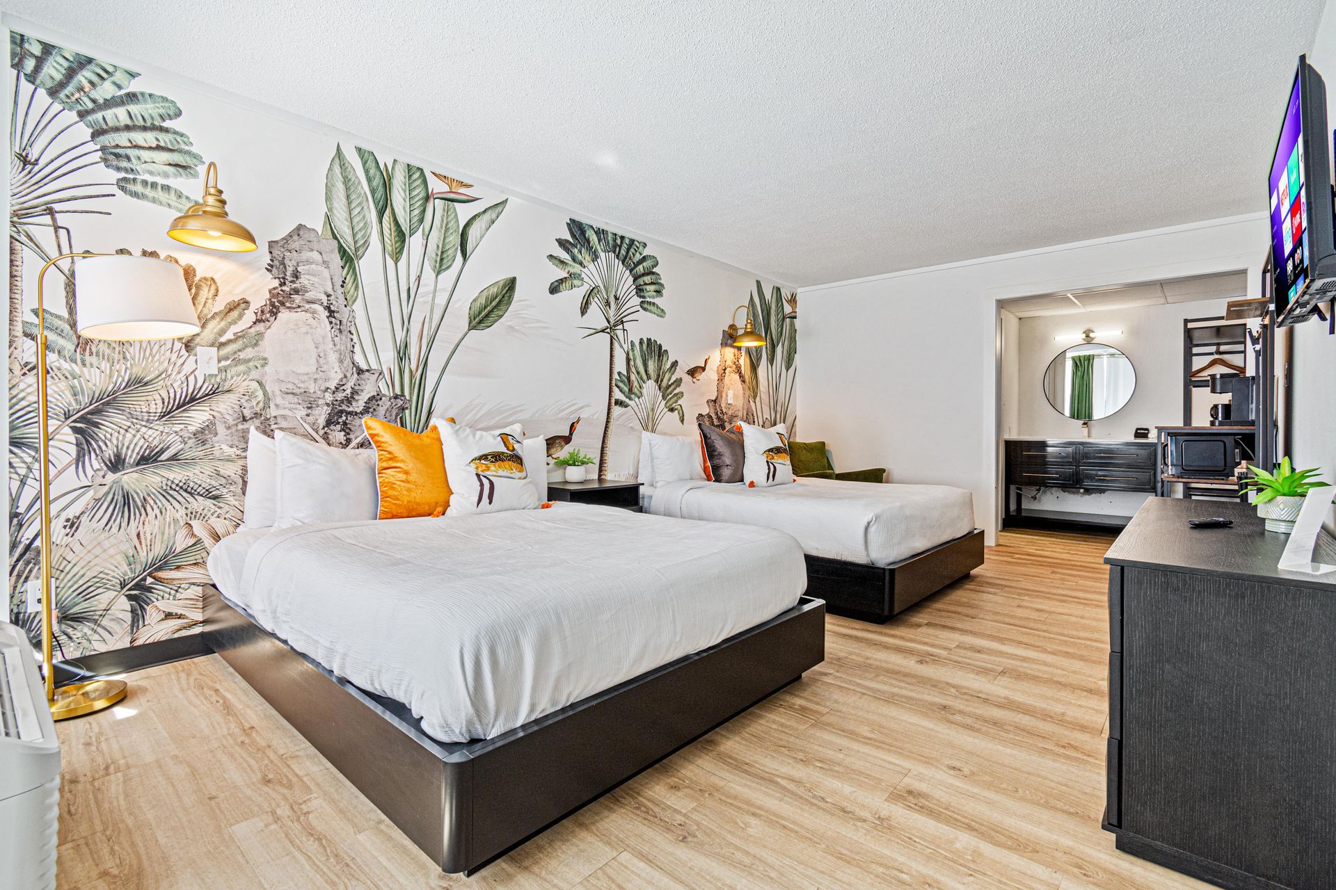 Hotel room with two beds, a tropical mural, and a TV.