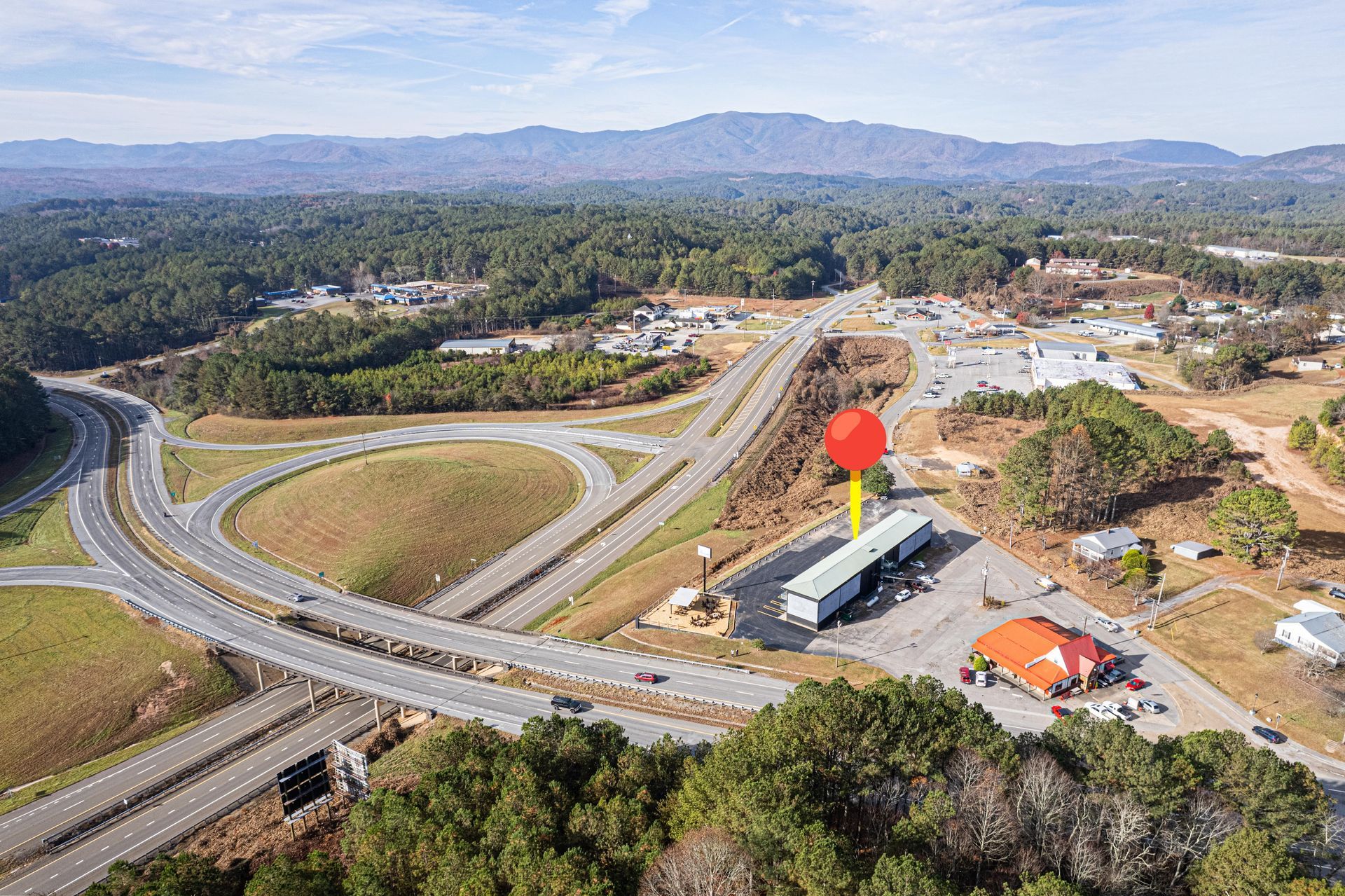 Aerial view of a highway interchange, mountains in the background, with a truck and gas station marked by a red pin.