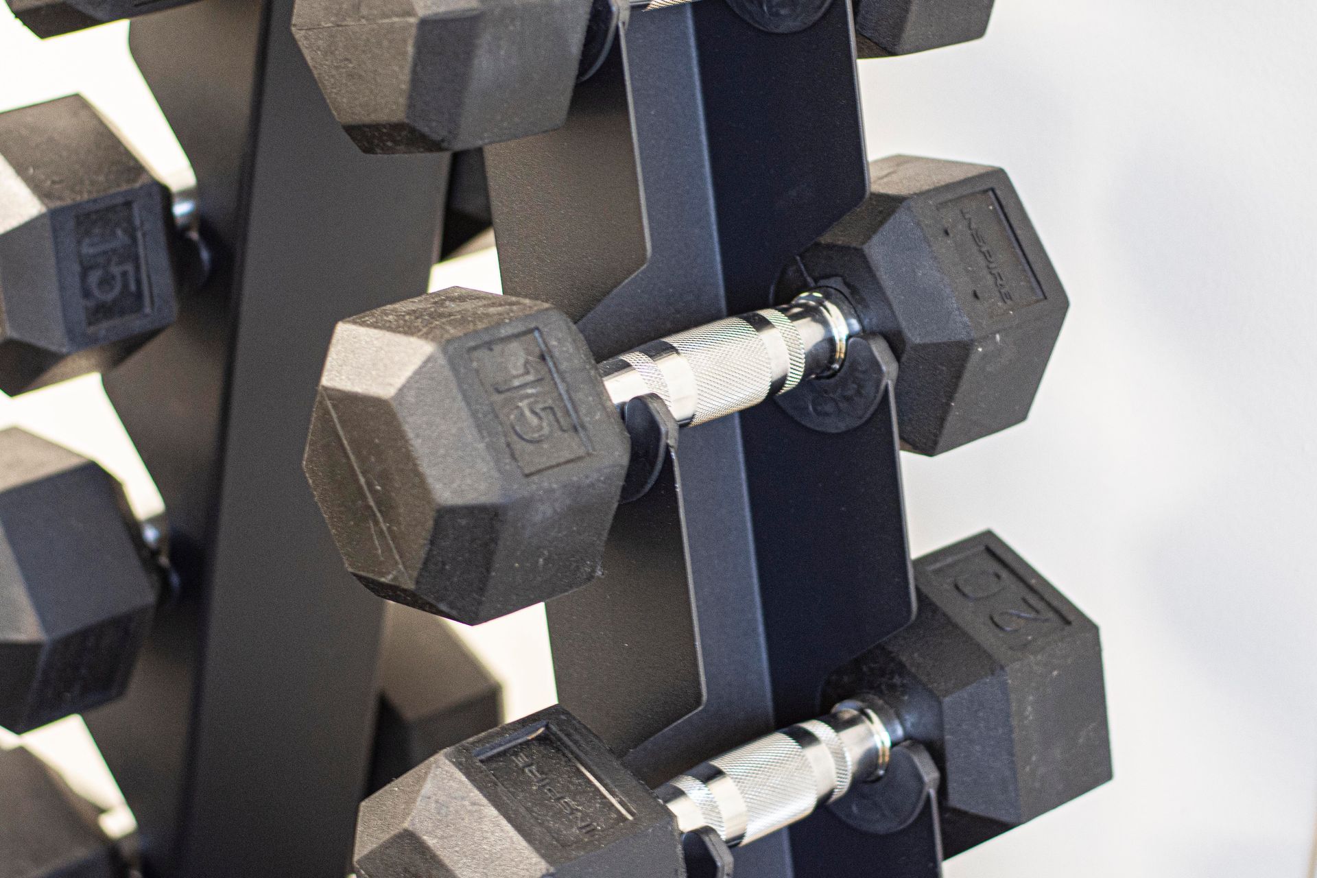 Black dumbbells on a black rack, various weights visible, in a gym setting.