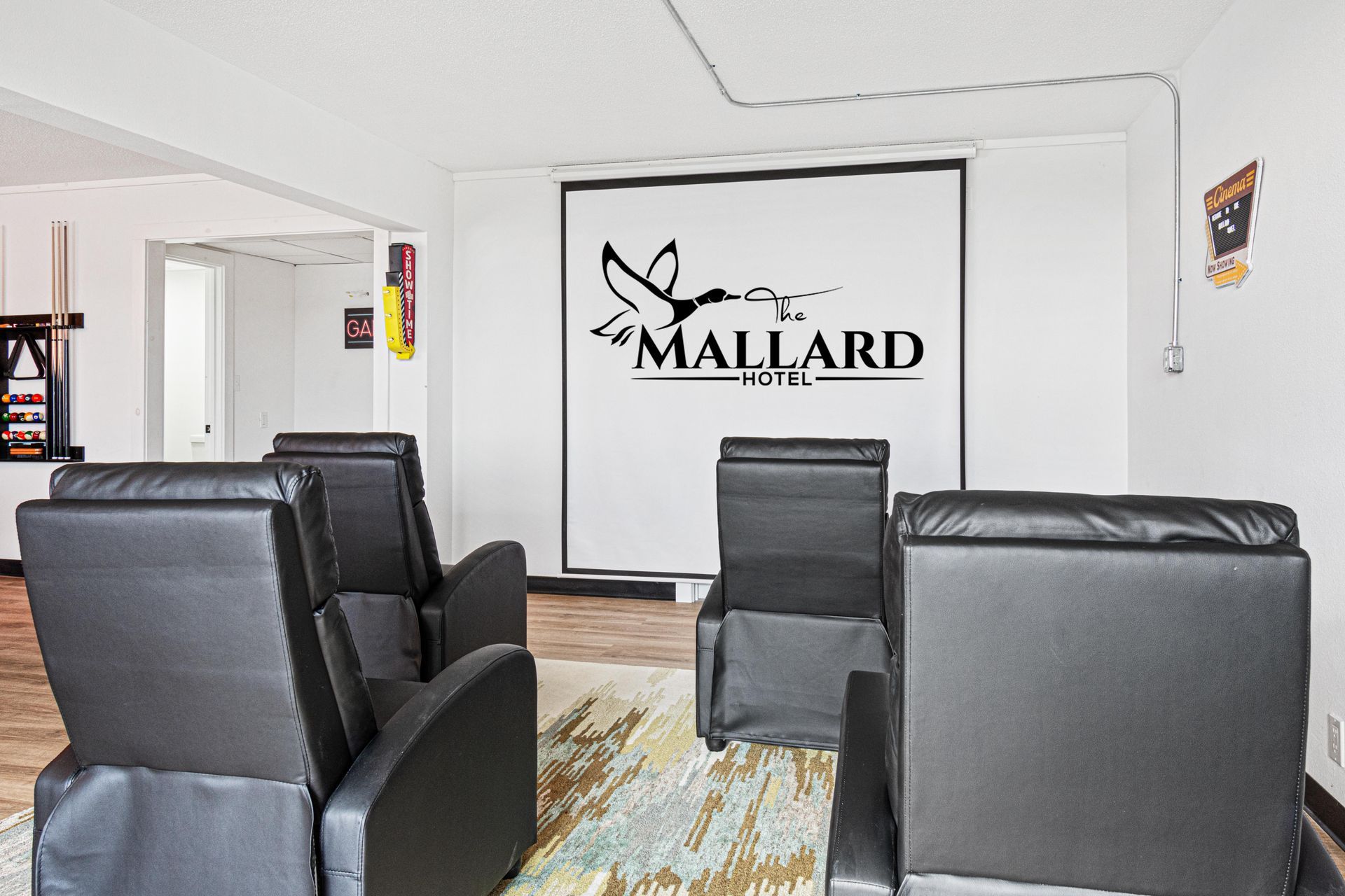 A media room with black recliners facing a screen with the Mallard logo.