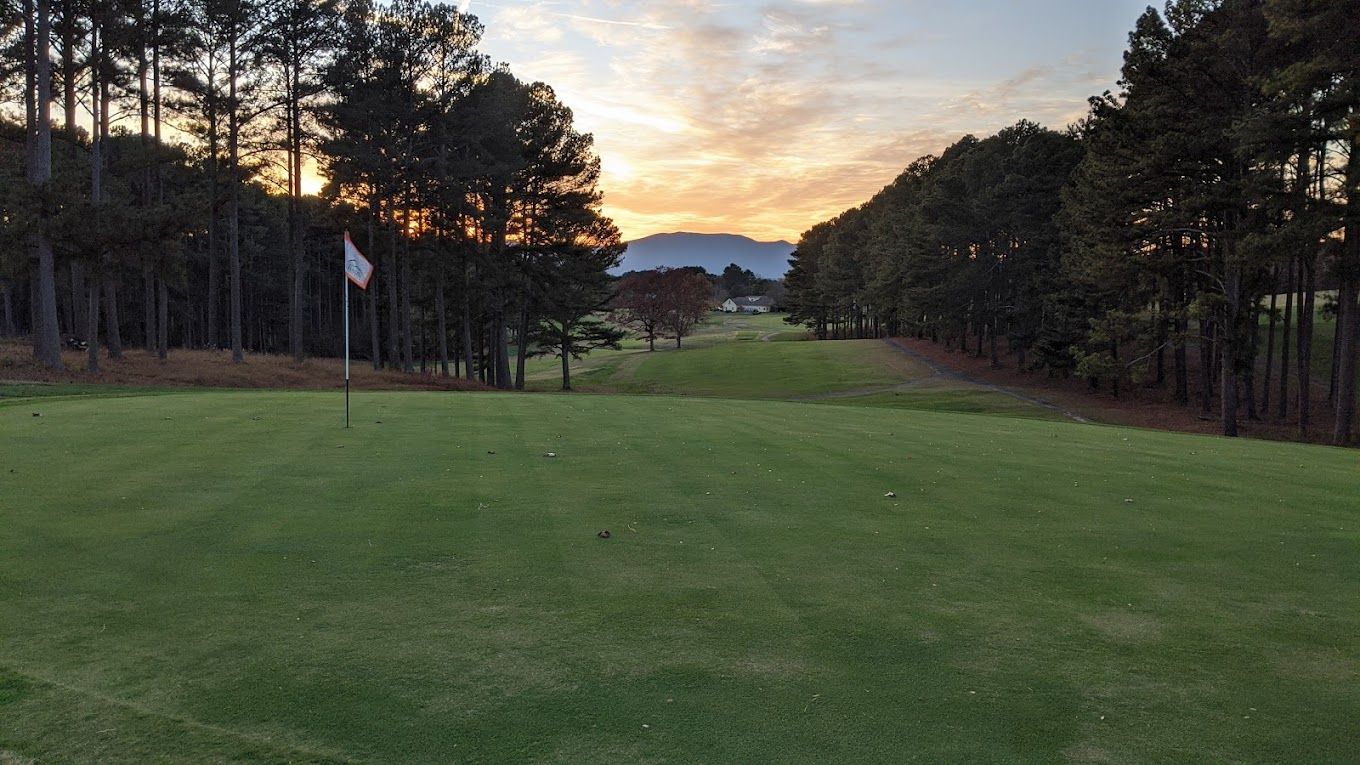 Golf course fairway with a setting sun, lined by trees.