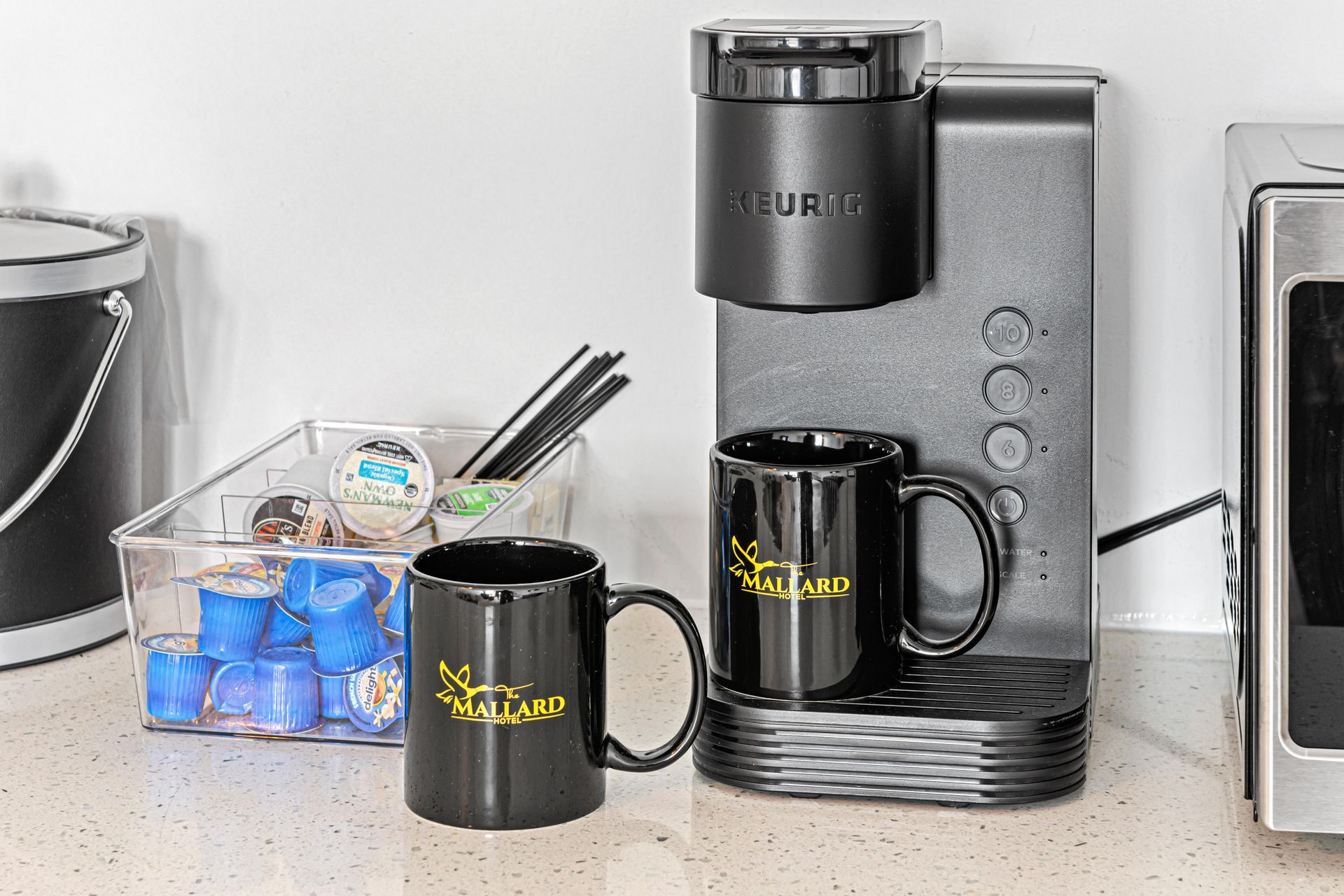 Keurig coffee maker with two black mugs, coffee pods, and supplies on a counter.