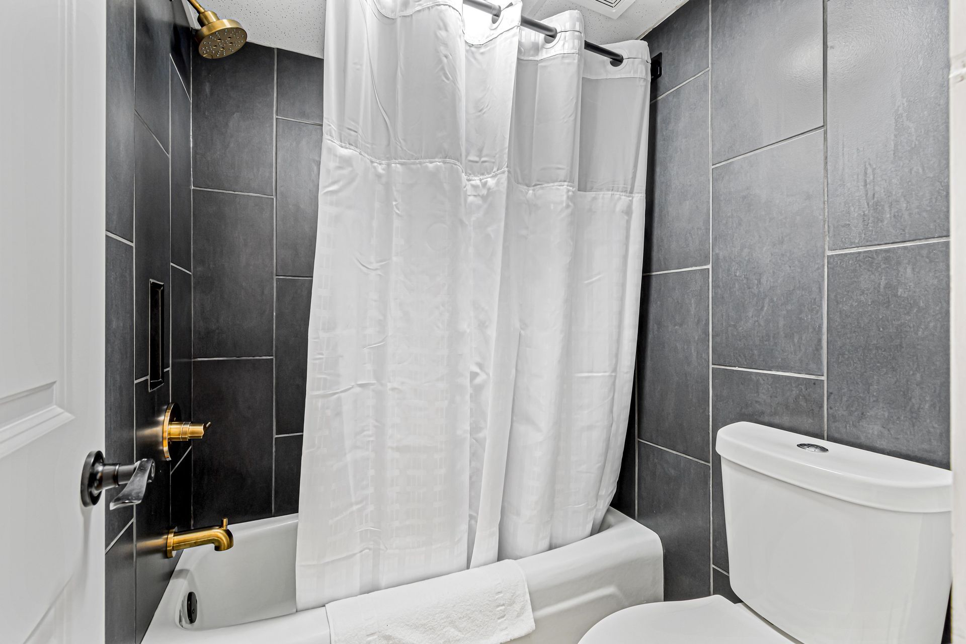 Bathroom with dark gray tile walls, white fixtures, and a white shower curtain.