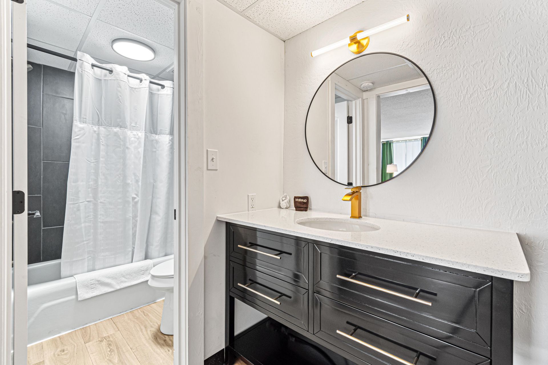 Bathroom with black vanity, round mirror, and shower with white curtain.
