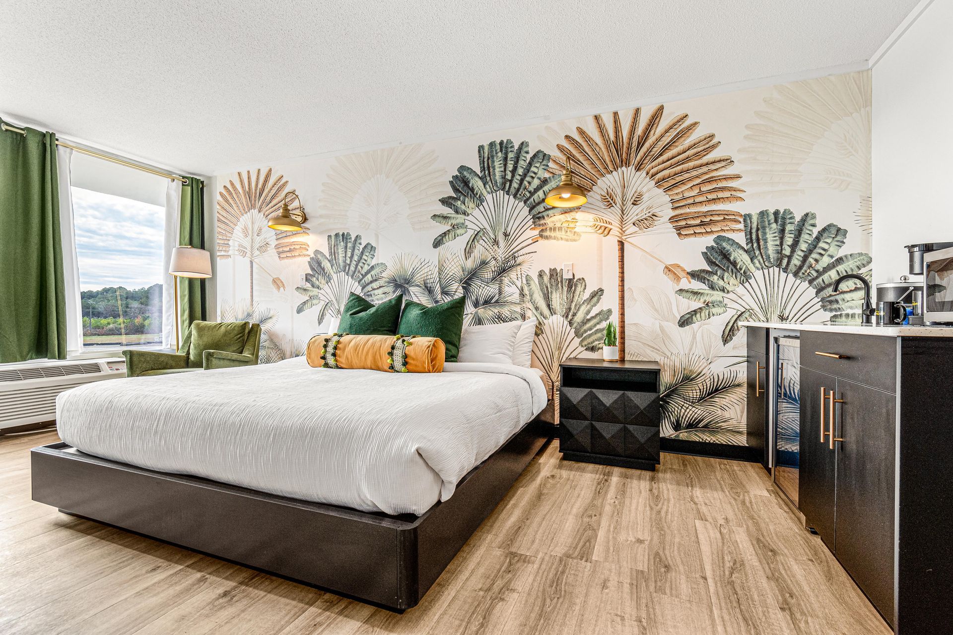 Hotel room with a bed, art, green accents, and a kitchenette.