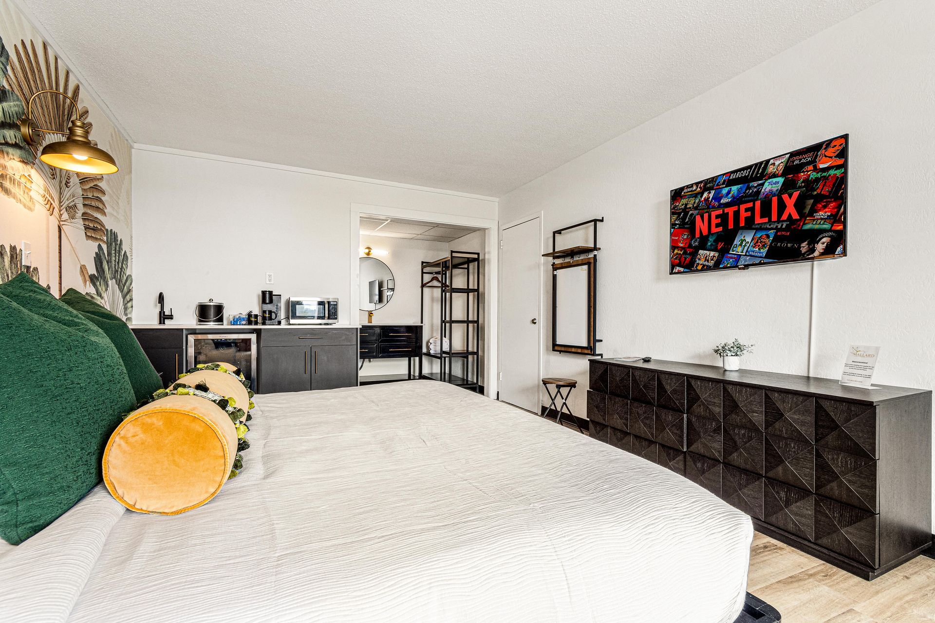 Bedroom with a large bed, TV, dresser, and a small kitchenette.