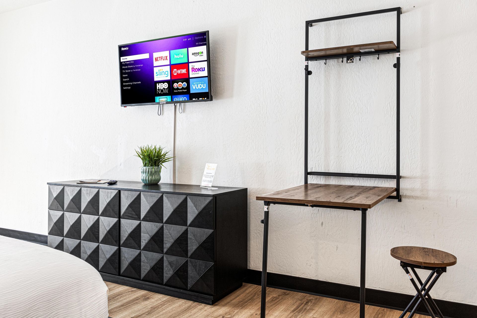 Bedroom with TV on wall, black dresser, and fold-out desk and stool.