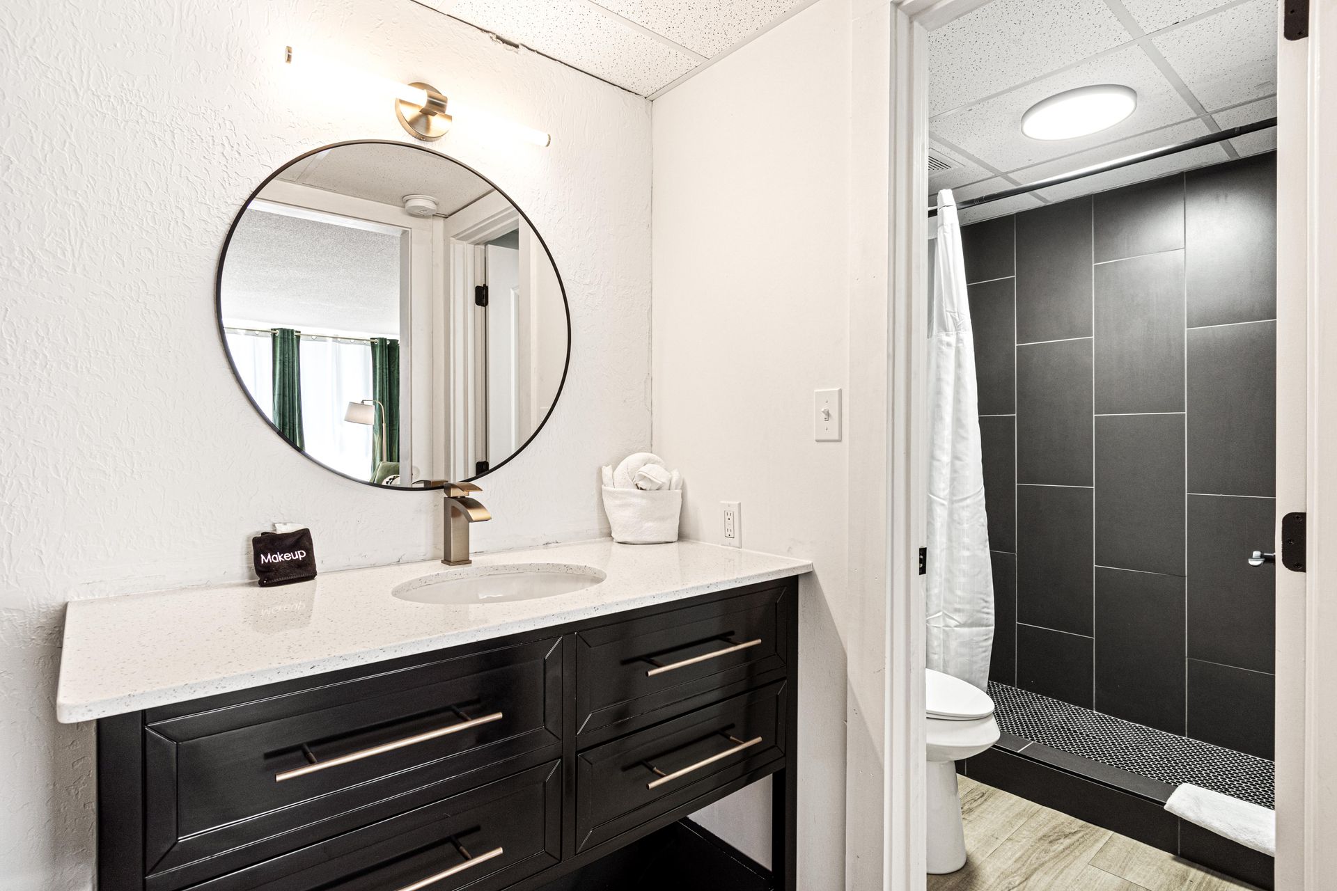 Bathroom with a black vanity, round mirror, and a walk-in shower with dark gray tiles.