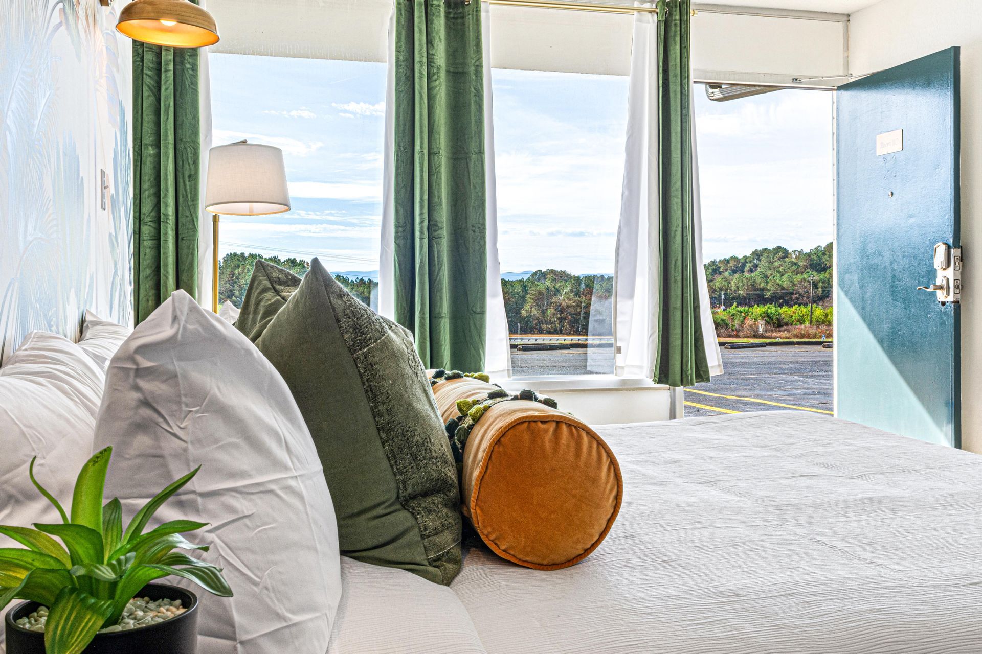 Bedroom with bed, green pillows, open door, green curtains, and view of outdoors.