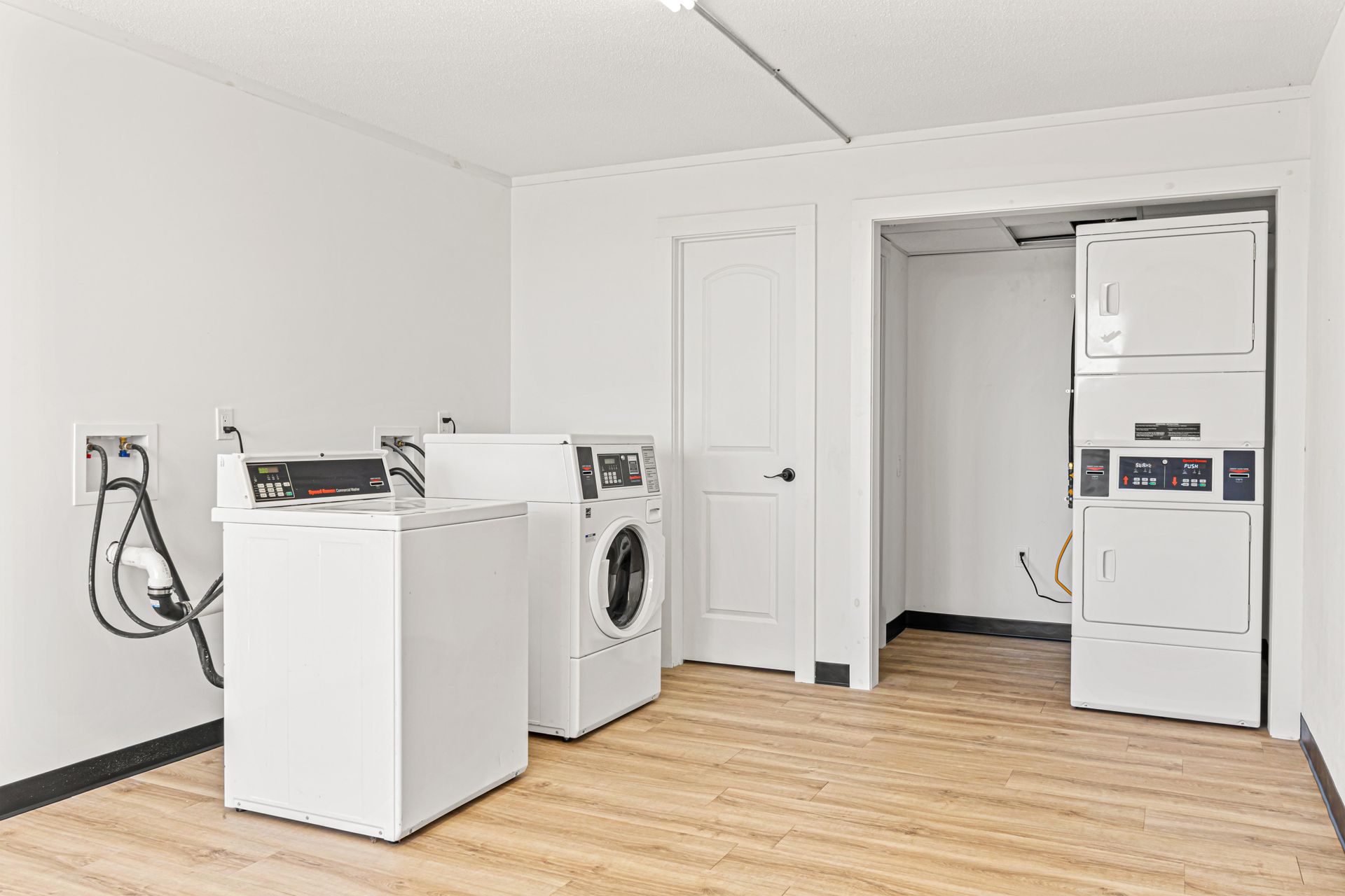 Laundry room with white machines, wooden floor, and white walls.